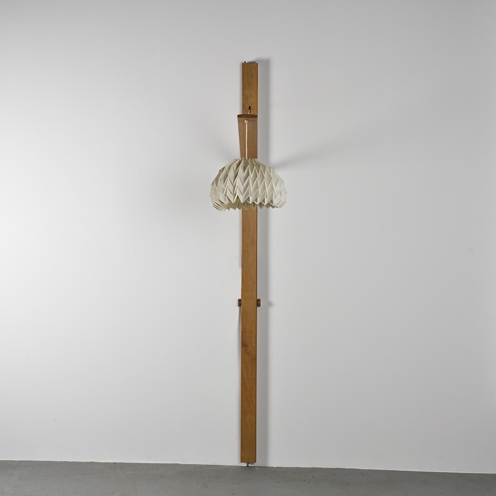 
Lampadaire en orme massif, composé d'une planche verticale supportant un bras lumineux réglable en hauteur grâce à un système de poulies. L'abat-jour, en papier plissé à effet nid d'abeille, diffuse une lumière douce et chaleureuse, contrastant