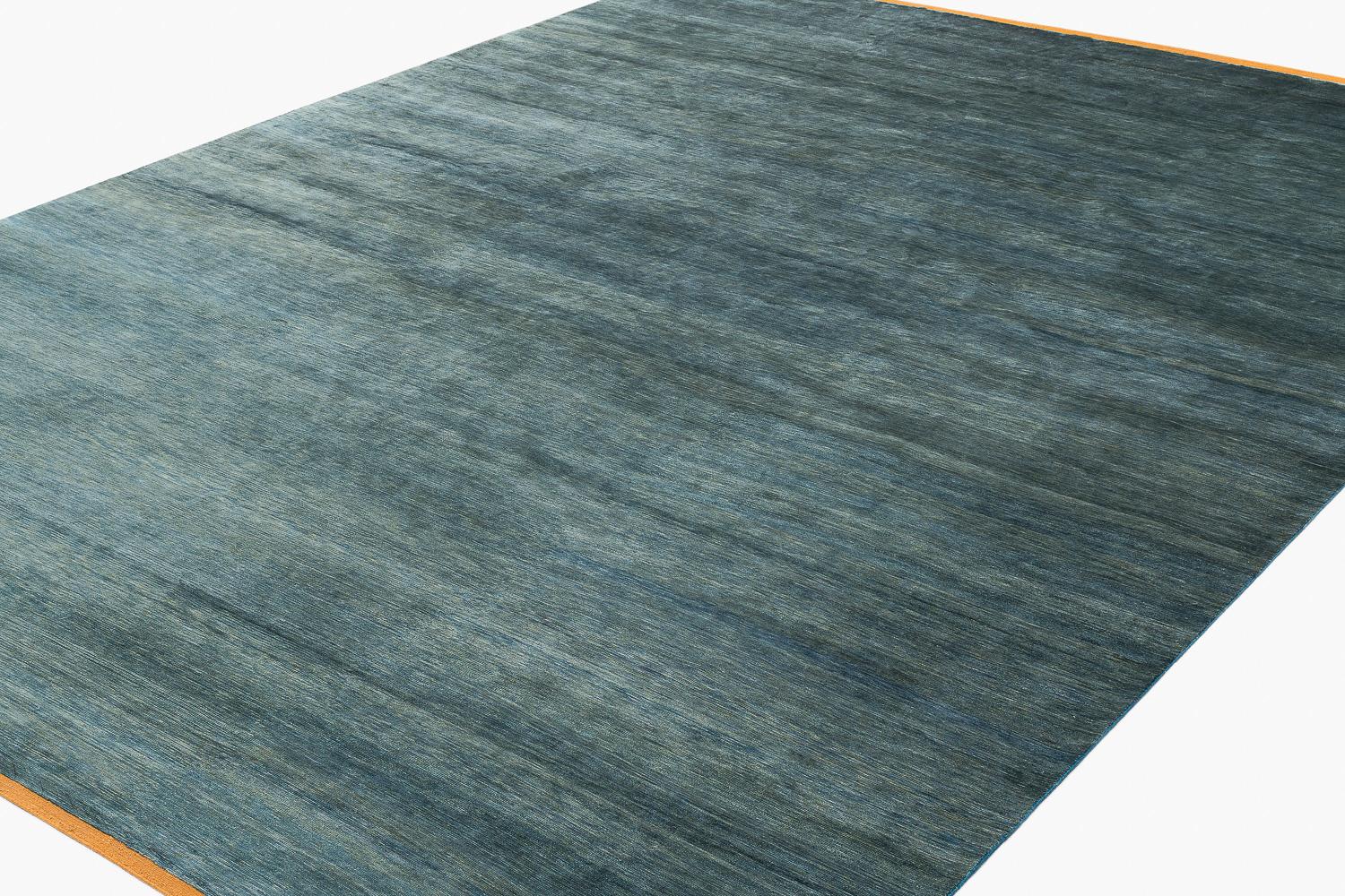 Esta alfombra de seda maciza se muestra en un verde misterioso y dinámico con toques de azul y gris. El estriado y la variedad natural en su color se consigue con tintes vegetales totalmente naturales, proporciona movimiento en toda la alfombra.