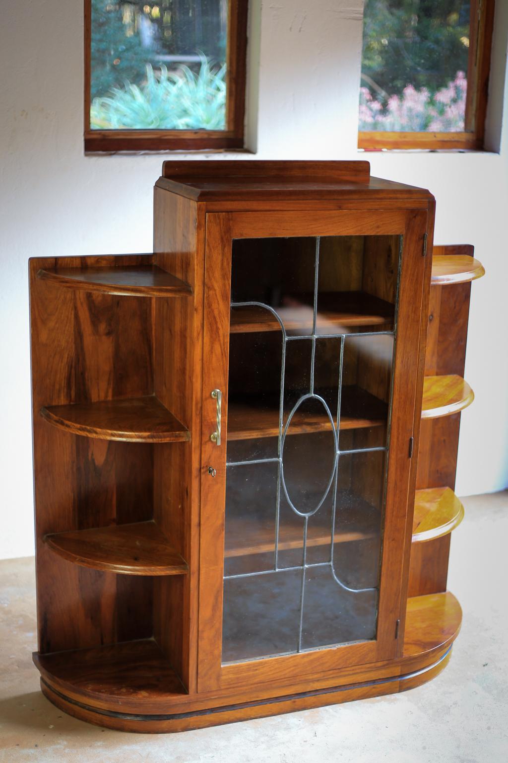 A solid mahogany Art Deco era book case and display cabinet in very good condition. It has a cabinet with three shelves and lead glass door. The cabinet is flanked with two curved open shelving sides. It is a heavy piece crafted with great skill. It
