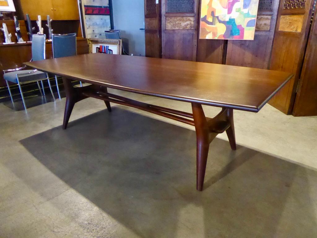 A solid mahogany dining table attributed to Monteverdi-Young, circa 1950s. The top is a curved rectangle and the spectacular base is distinguished by an over-scale Hans Wegner style wishbone stretcher that resolves as a through-tenon. The table has