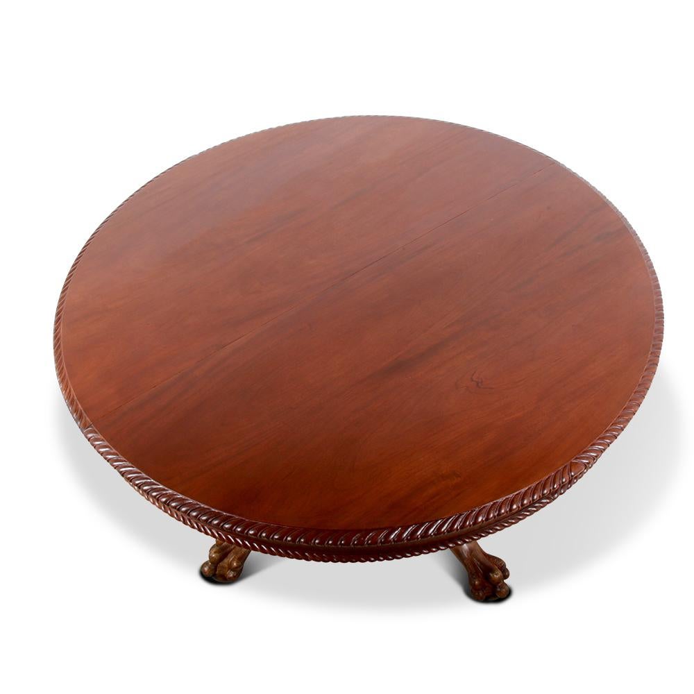 A British-made solid mahogany round dining table with four original matching leaves. An extremely well-build table, having a well-carved Chippendale style base, the four legs with acanthus leaf details and paw feet, the mahogany plank top and leaves