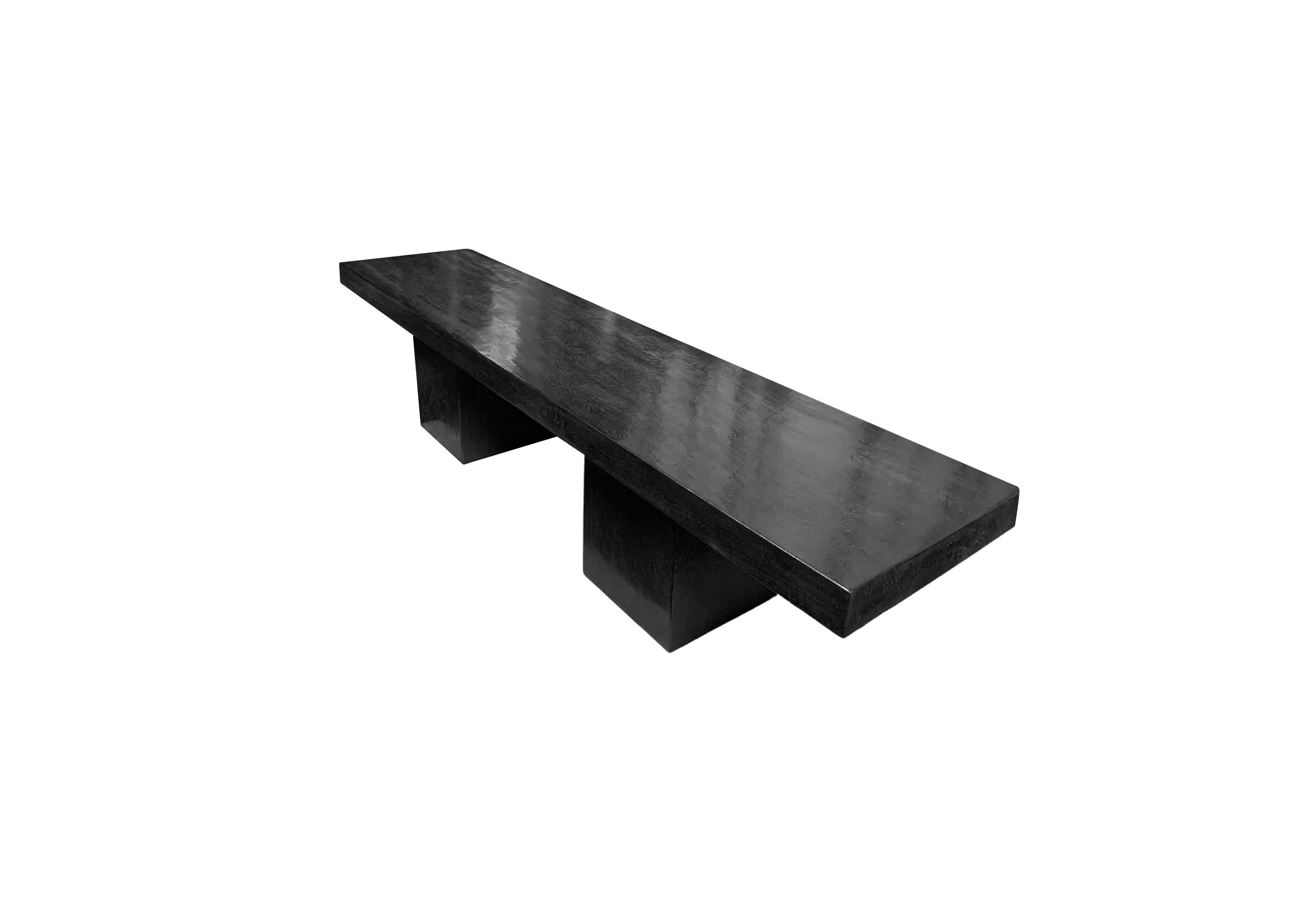 A sculptural mango wood bench. To achieve is rich black pigment the bench was burnt three times and then finished with a clear coat. The seat was crafted from a solid block of mango wood. The seat sits atop two solid, square legs. A wonderfully