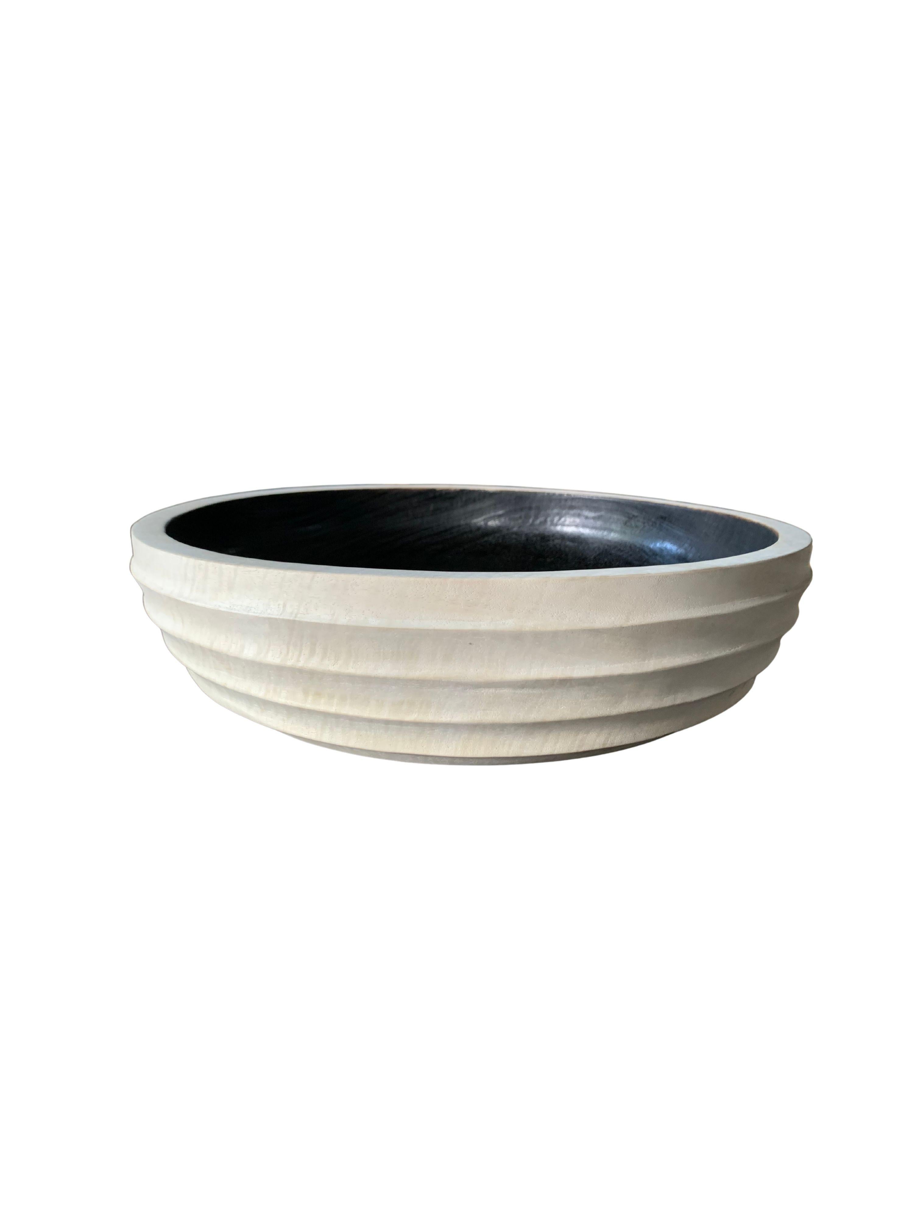 A hand-crafted mango wood bowl. The bowl was cut from a much larger slab of mango wood and features a ribbed texture on its sides. Unique to this bowl are the mix of bleached and burnt finishes. The outter exterior of the bowl features a bleached