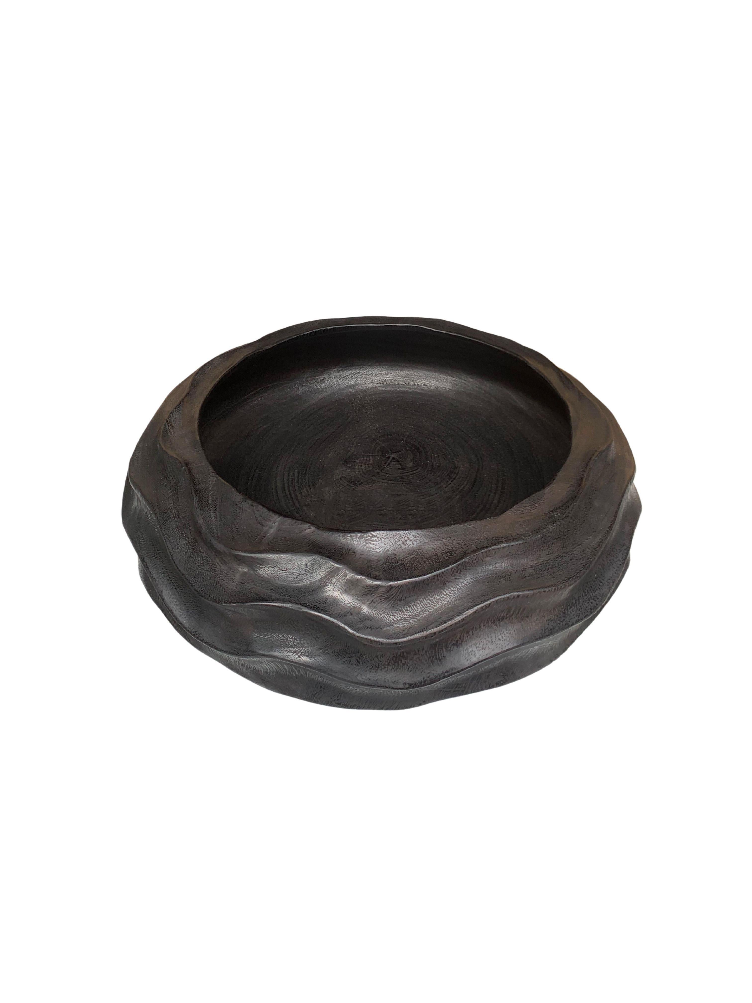 A hand-crafted mango wood bowl. The bowl was cut from a much larger slab of mango wood and features a curved and ribbed texture on its sides. To achieve its rich black colour the bowl was burnt three times and finished with a clear coat. A