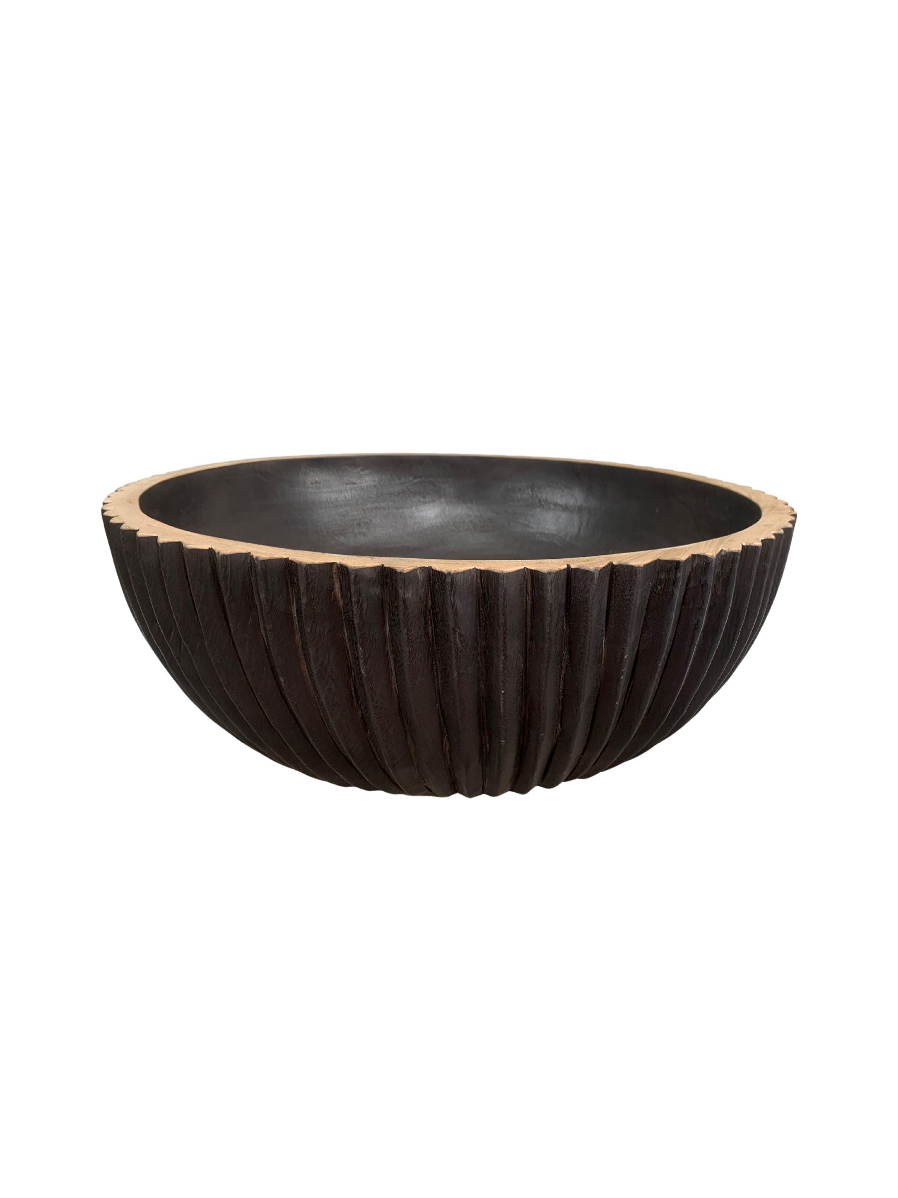 A hand-crafted mango wood bowl. The bowl was cut from a much larger slab of mango wood and features a ribbed texture on its sides. To achieve the rich black colour the bowl was burnt three times and finished with a clear coat. The rim was then