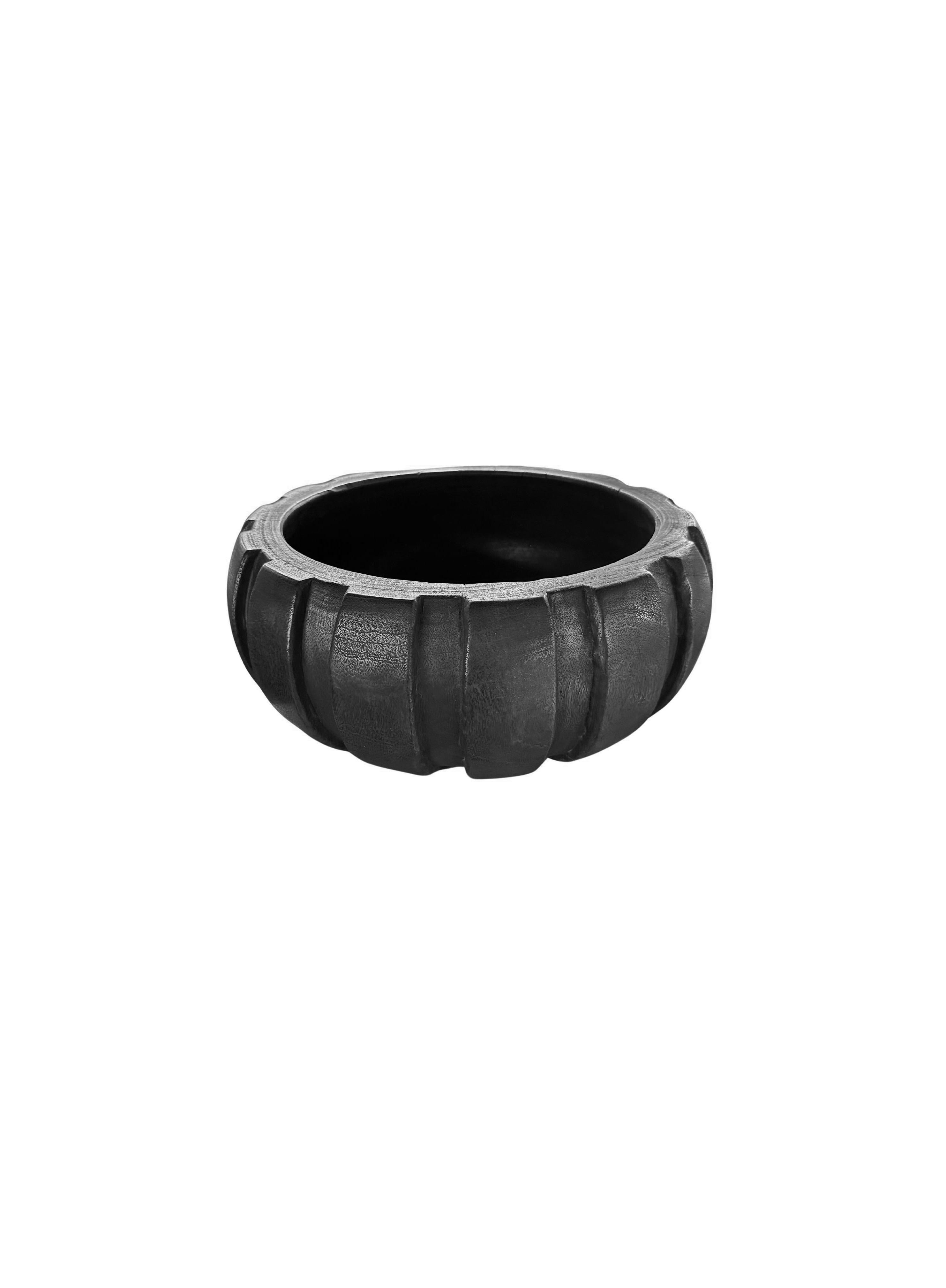 Un cuenco de madera de mango hecho a mano. El cuenco se cortó de una plancha mucho mayor de madera de mango y presenta una textura curvada y estriada en los lados. Para conseguir su intenso color negro, el cuenco se quemó tres veces y se terminó con
