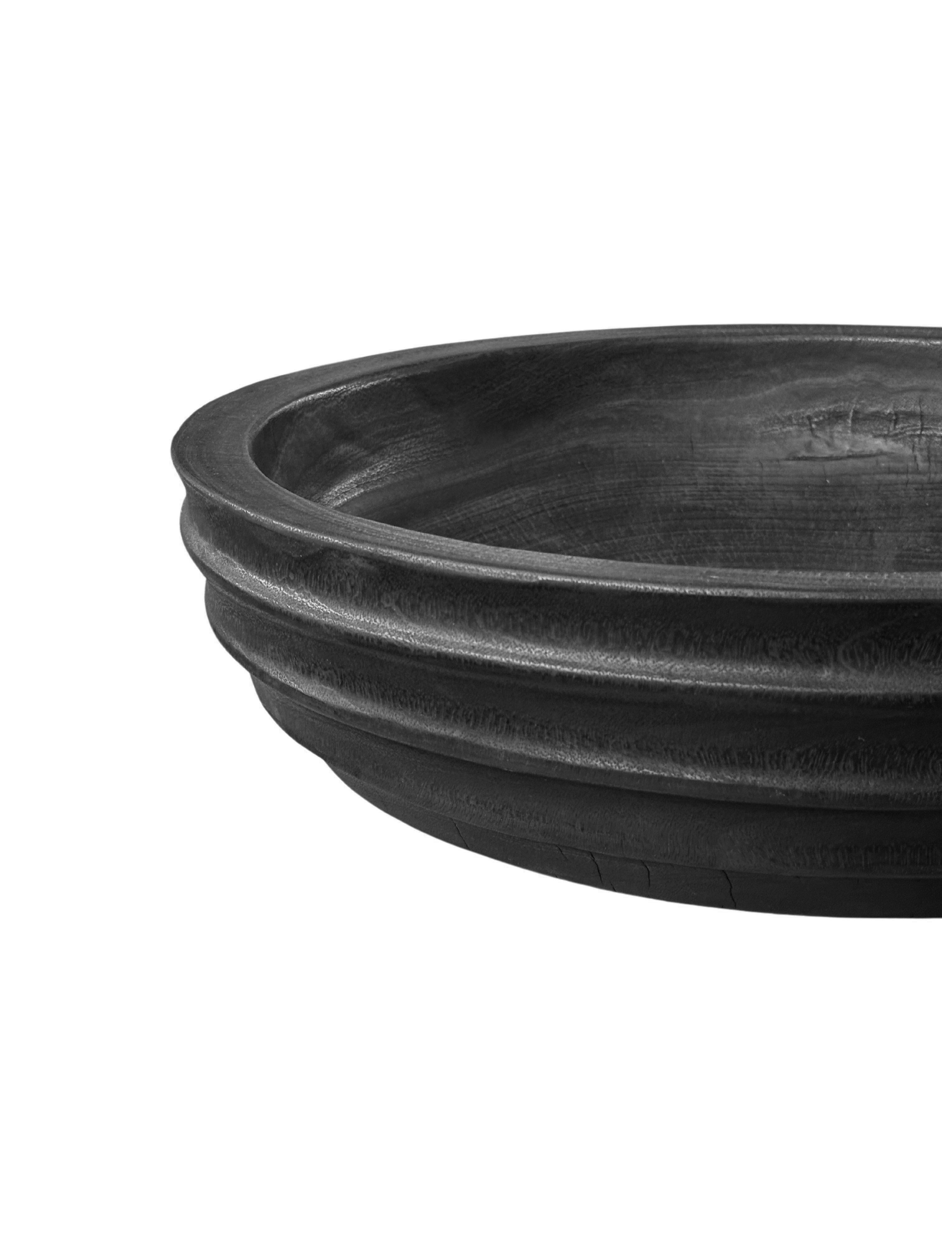 A hand-crafted mango wood bowl. The bowl was cut from a much larger slab of mango wood and features a curved and ribbed texture on its sides. To achieve its rich black colour the bowl was burnt three times and finished with a clear coat. A