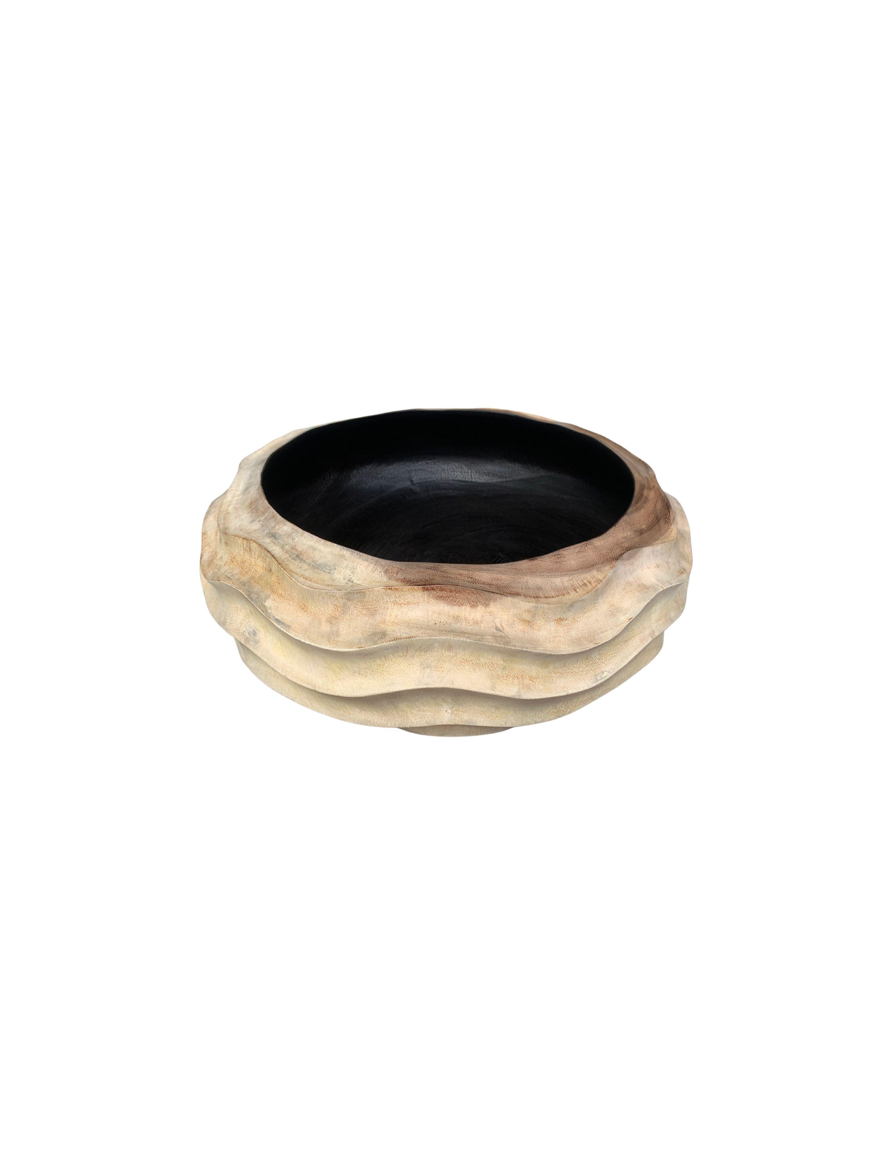 A hand-crafted mango wood bowl. The bowl was cut from a much larger slab of mango wood and features a curved and ribbed texture on its sides. The bowl is contrasted by an exterior that features a natural finish and a basin that features a burnt