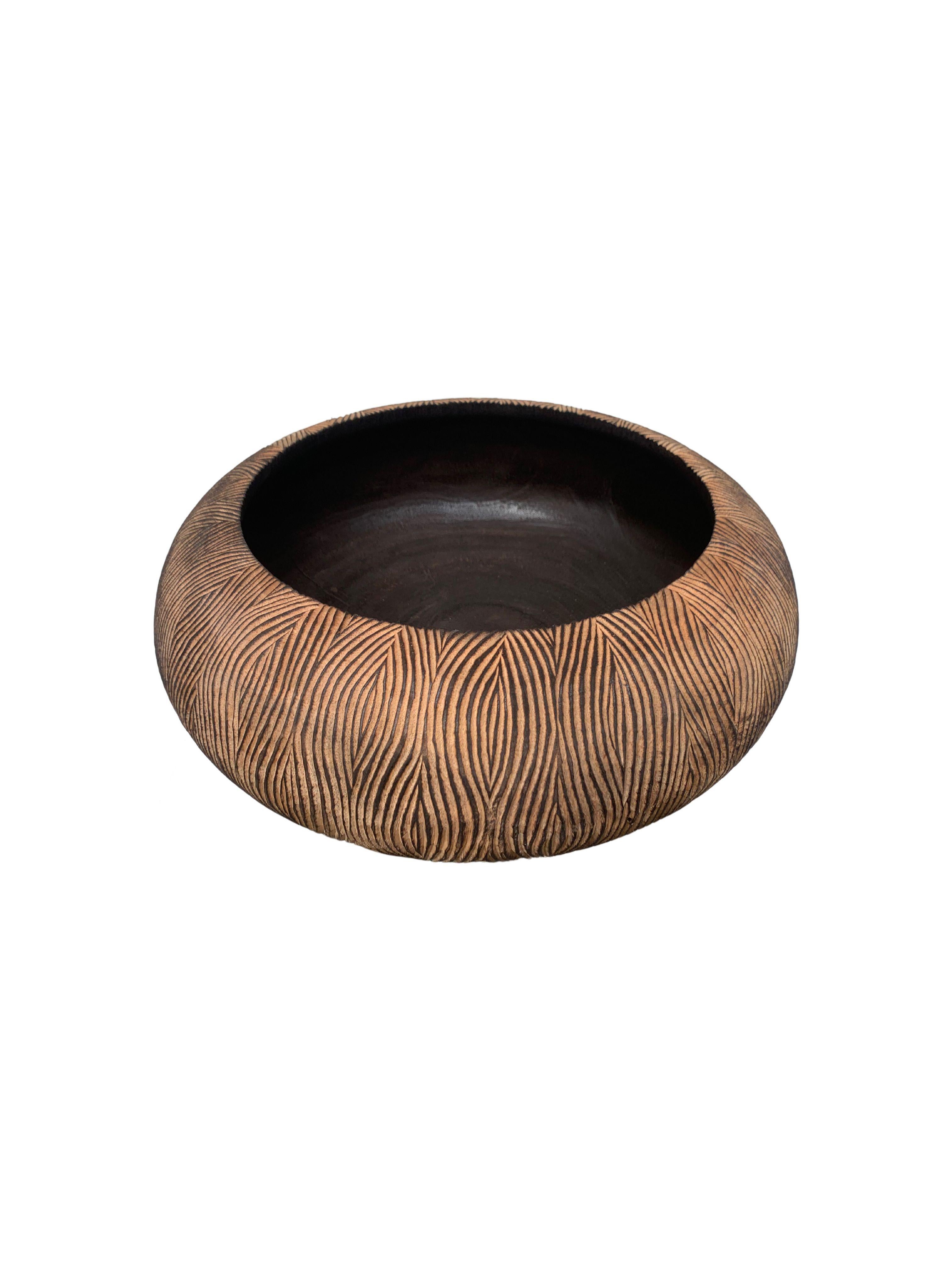 A hand-crafted mango wood bowl. The bowl was cut from a much larger slab of mango wood and features a hand carved texture on its sides. This bowl was burnt three times to achieve its rich black colour present in its basin. The exterior was then