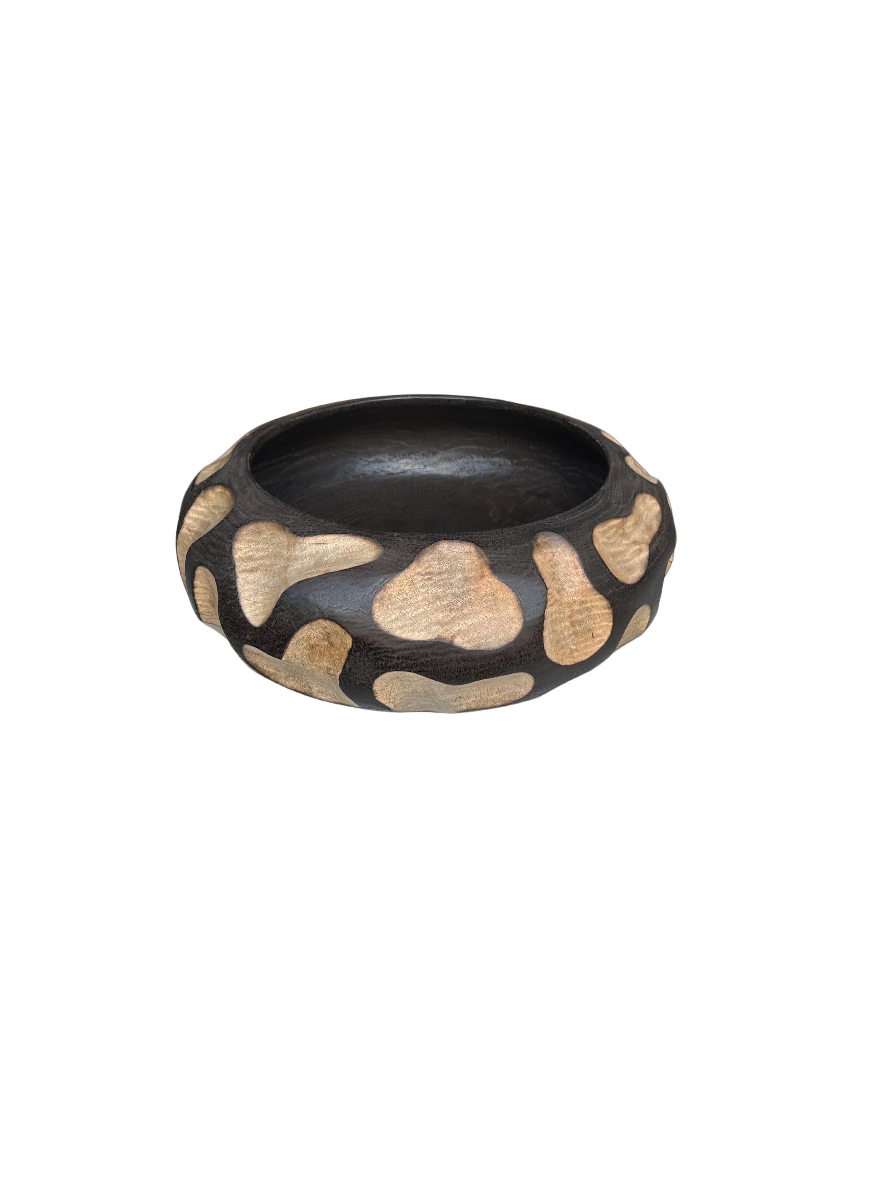A hand-crafted mango wood bowl. The bowl was cut from a much larger slab of mango wood and features a hand-carved texture on its sides. To achieve the black color the wood was burnt several times and finished with a clear coat. The mix of natural