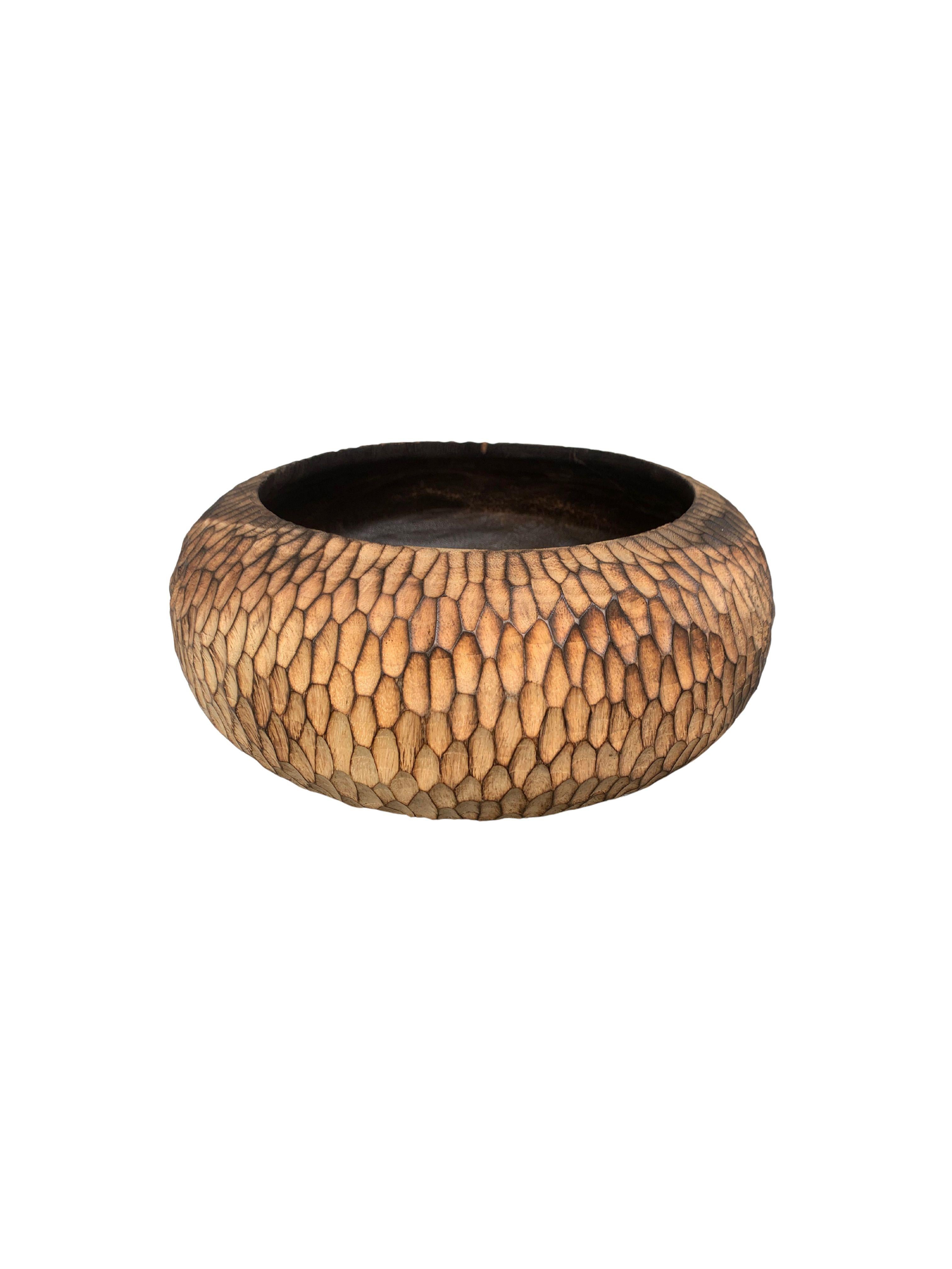 A hand-crafted mango wood bowl. The bowl was cut from a much larger slab of mango wood and features a hand-hewn texture on its sides. This bowl was burnt three times to achieve its rich black colour present in its basin. The exterior was then slowly