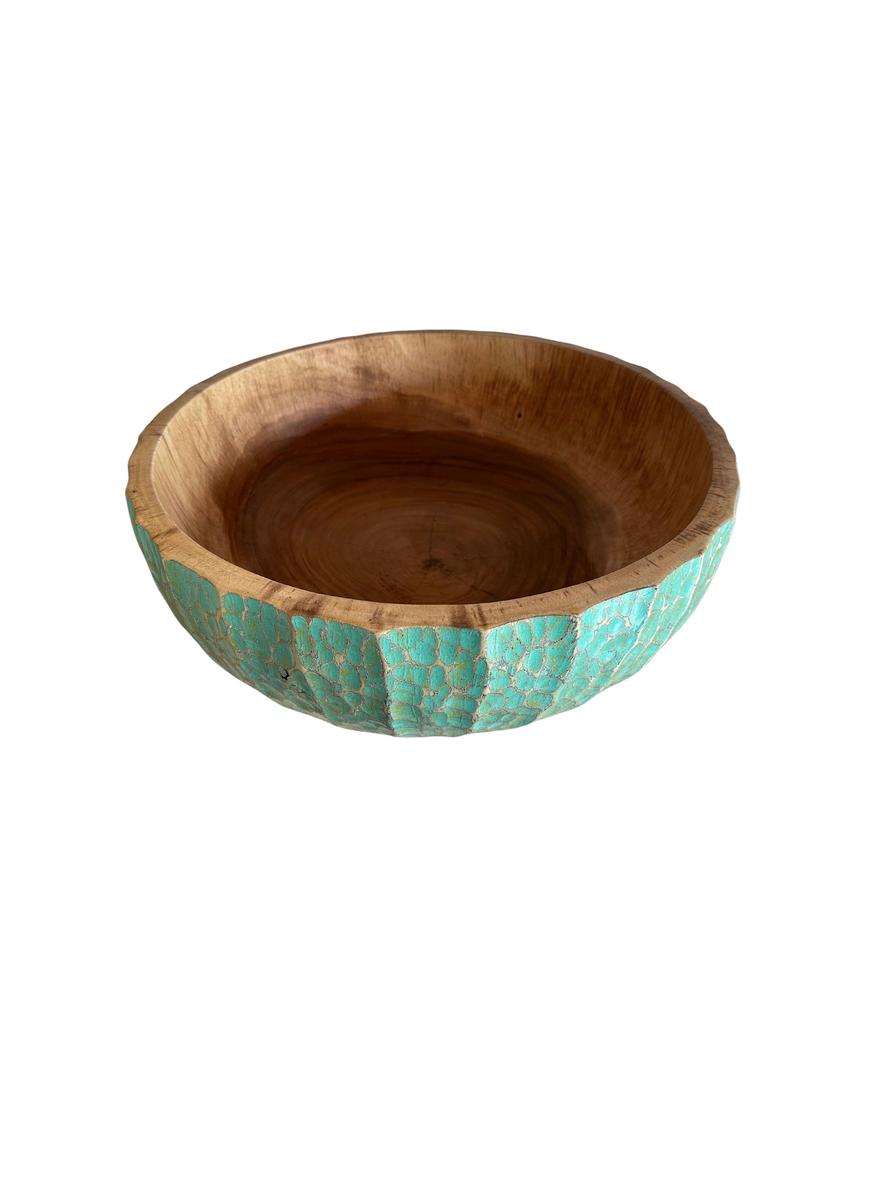 A hand-crafted mango wood bowl. The bowl was cut from a much larger slab of mango wood and features a hand painted detailing on its sides that is then sanded down to achieve a unique texture. This bowl also features hand-carved detailing providing