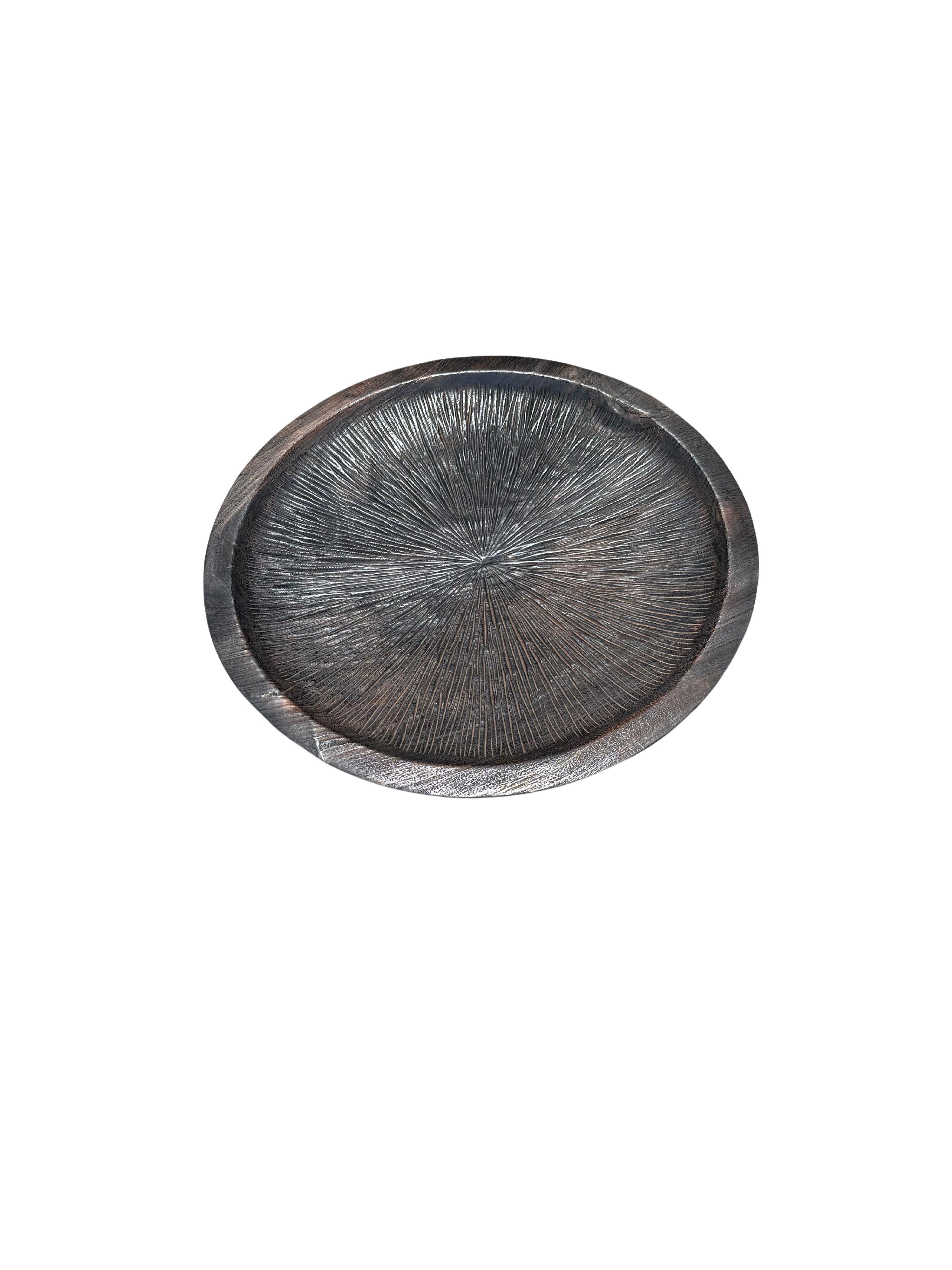 A hand-crafted mango wood bowl. The bowl was cut from a much larger slab of mango wood and features a hand carved detailing along its basin It maintains a wonderful wood texture and shades. To achieve its brown colour the wood was burned several