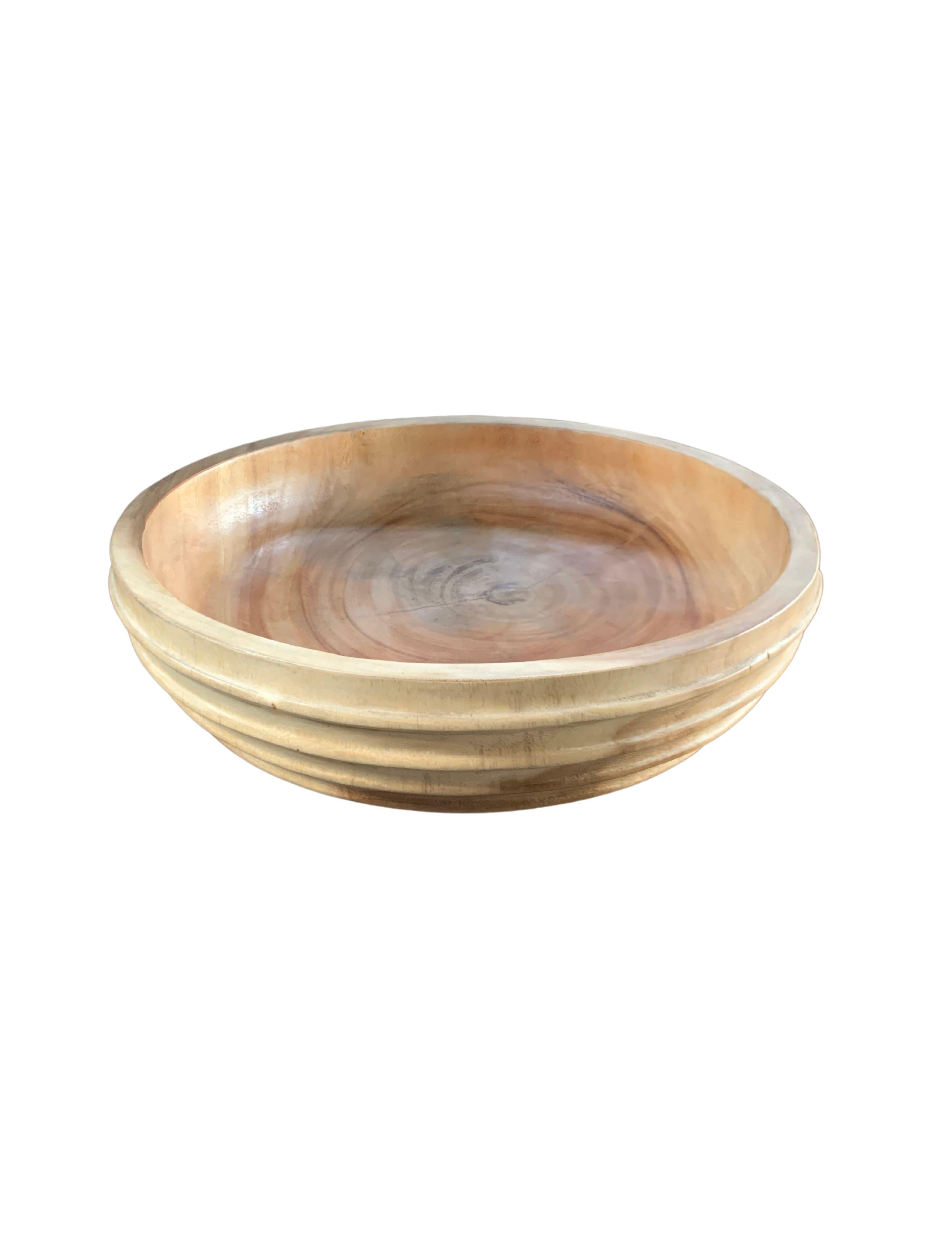 A hand-crafted mango wood bowl. The bowl was cut from a much larger slab of mango wood and features a ribbed texture on its sides. The bowl has been meticulously sanded down to achieve a wonderful smooth texture. The bowl is then completed with a