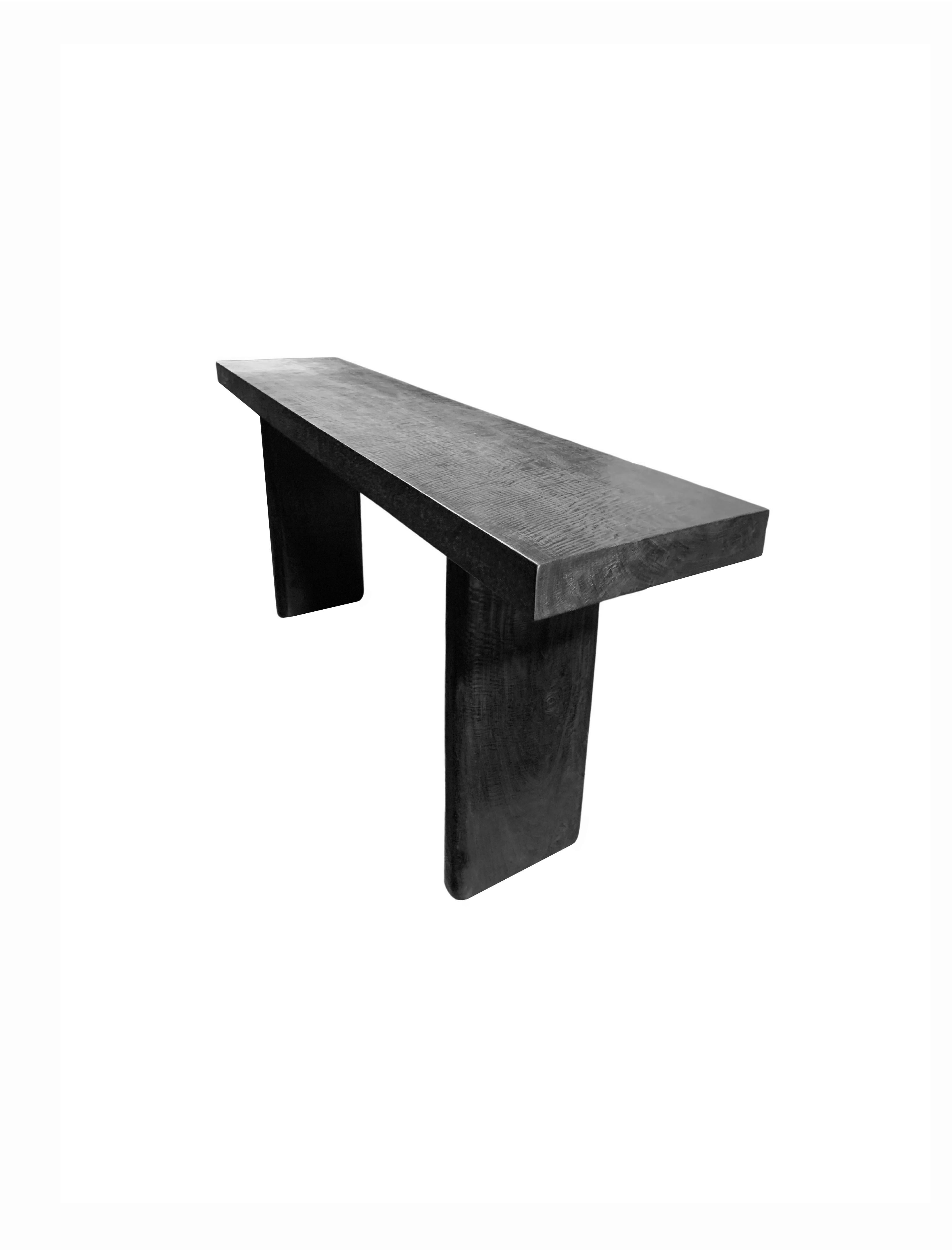 A sculptural mango wood console table. To achieve is rich black pigment the bench was burnt three times and then finished with a clear coat. The table was crafted from a solid block of mango wood. The table top sits atop two solid, narrow legs. The