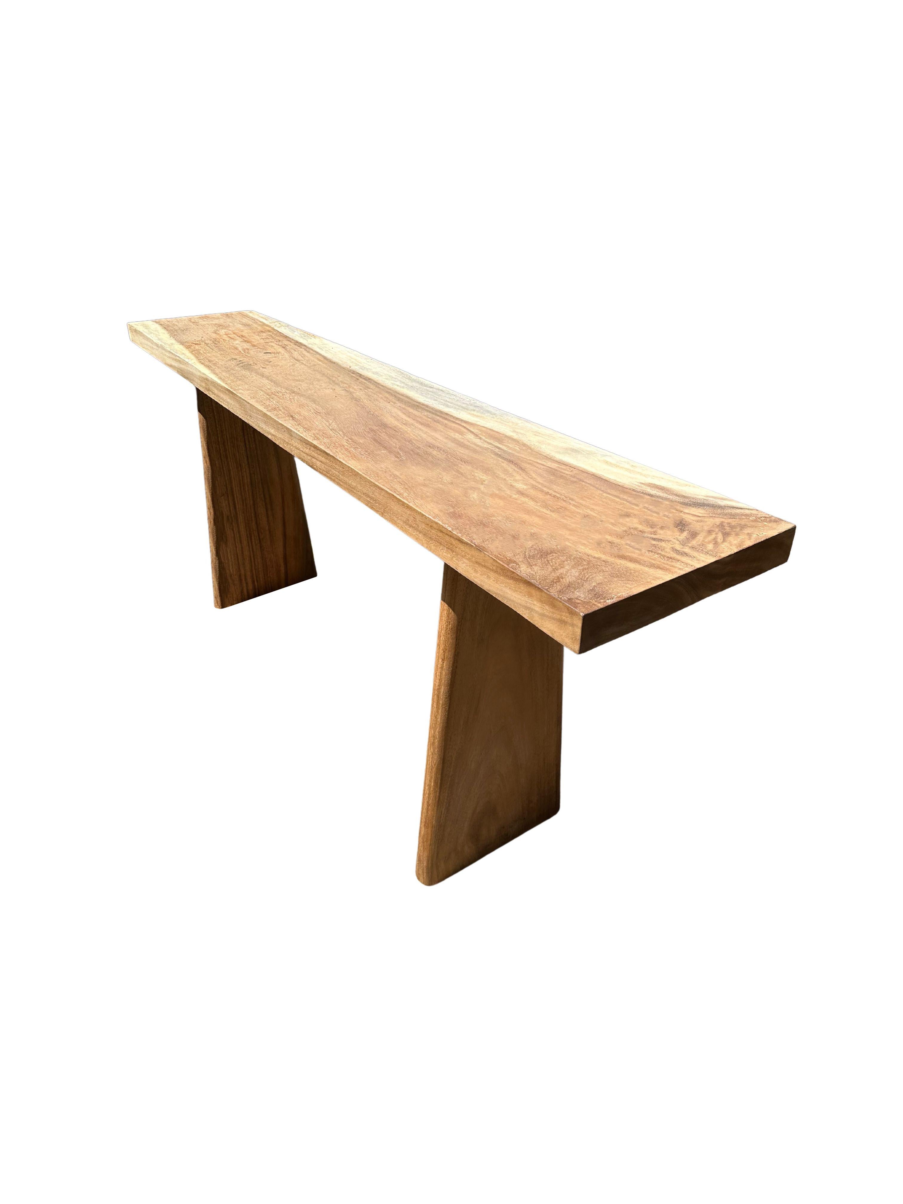 A sculptural mango wood console table crafted from solid mango wood. The table top sits atop two solid, narrow legs. The tables legs are angular and feature curved edges providing a wonderful mix of curved and straight lines to the table. A