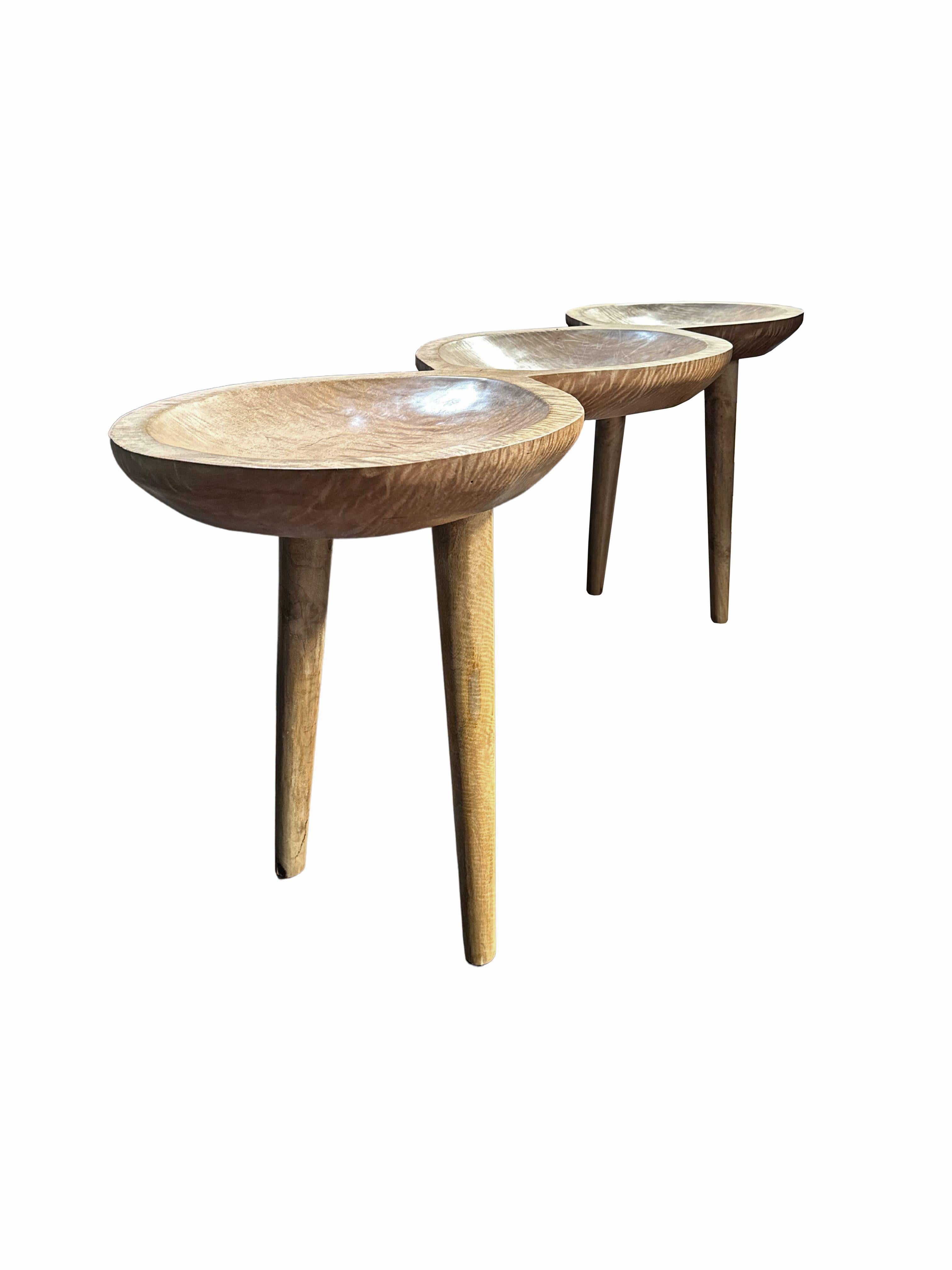 A sculptural mango wood console table crafted from solid mango wood. The table top sits atop four slender legs. The tables legs are angular and feature curved edges providing a wonderful mix of curved and straight lines to the table. The subtle wood