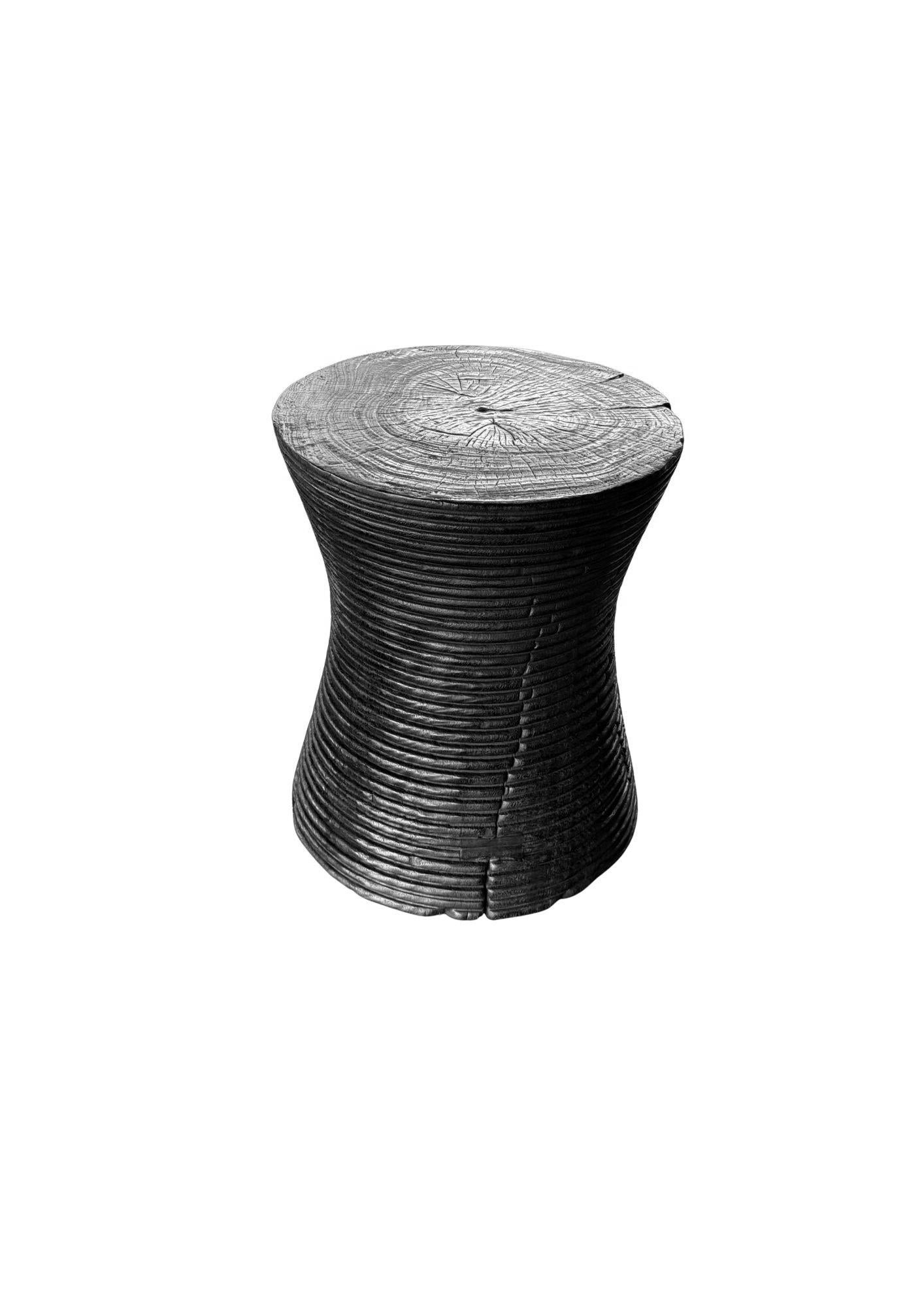 Fabriquée en bois de manguier massif, cette table d'appoint sculpturale présente une finition unique, brûlée à la main, obtenue par de multiples couches de carbonisation contrôlée. Le processus de combustion répété met en valeur le grain et la