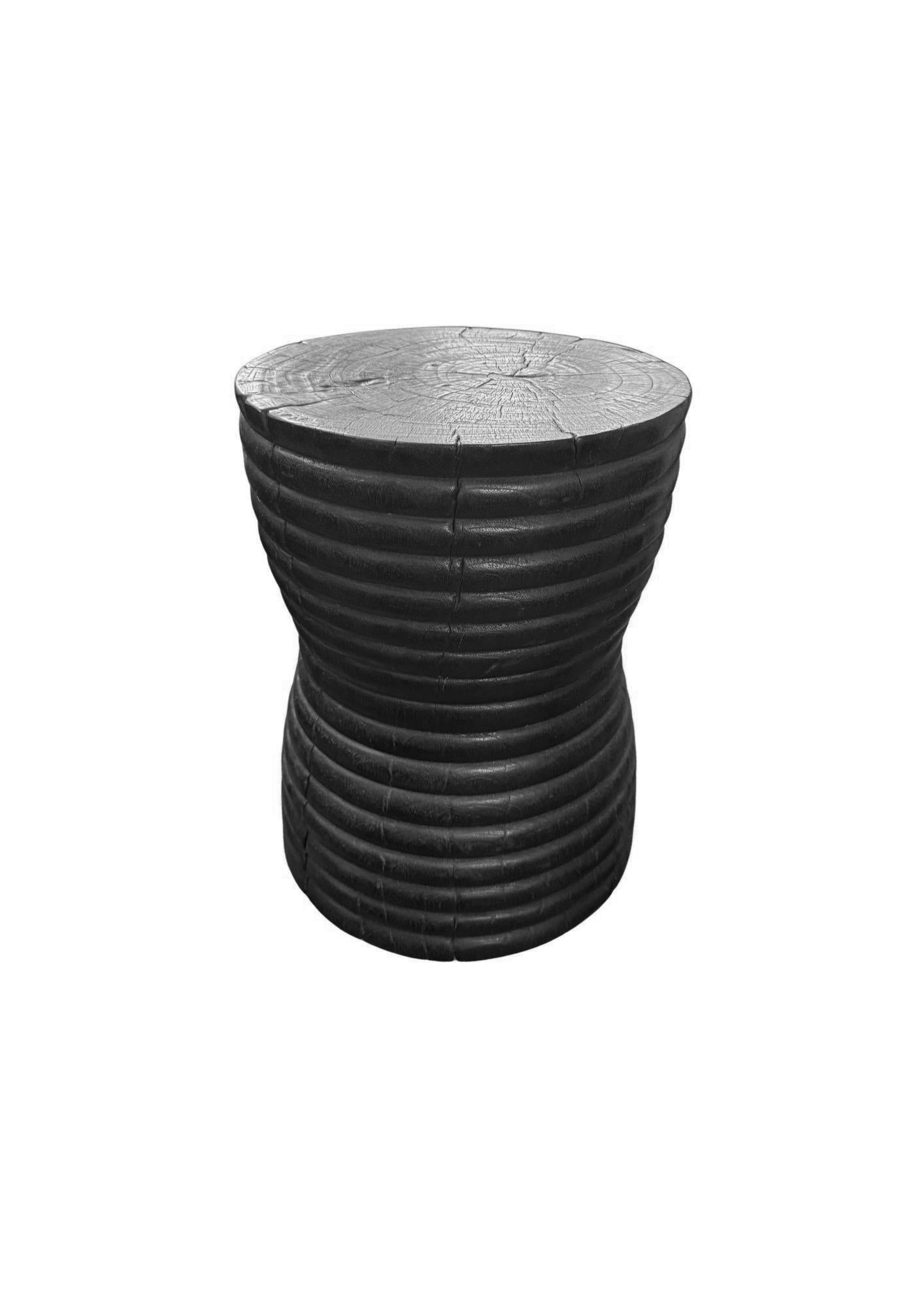 Fabriquée en bois de manguier massif, cette table d'appoint sculpturale présente une finition unique, brûlée à la main, obtenue par de multiples couches de carbonisation contrôlée. Le processus de combustion répété met en valeur le grain et la