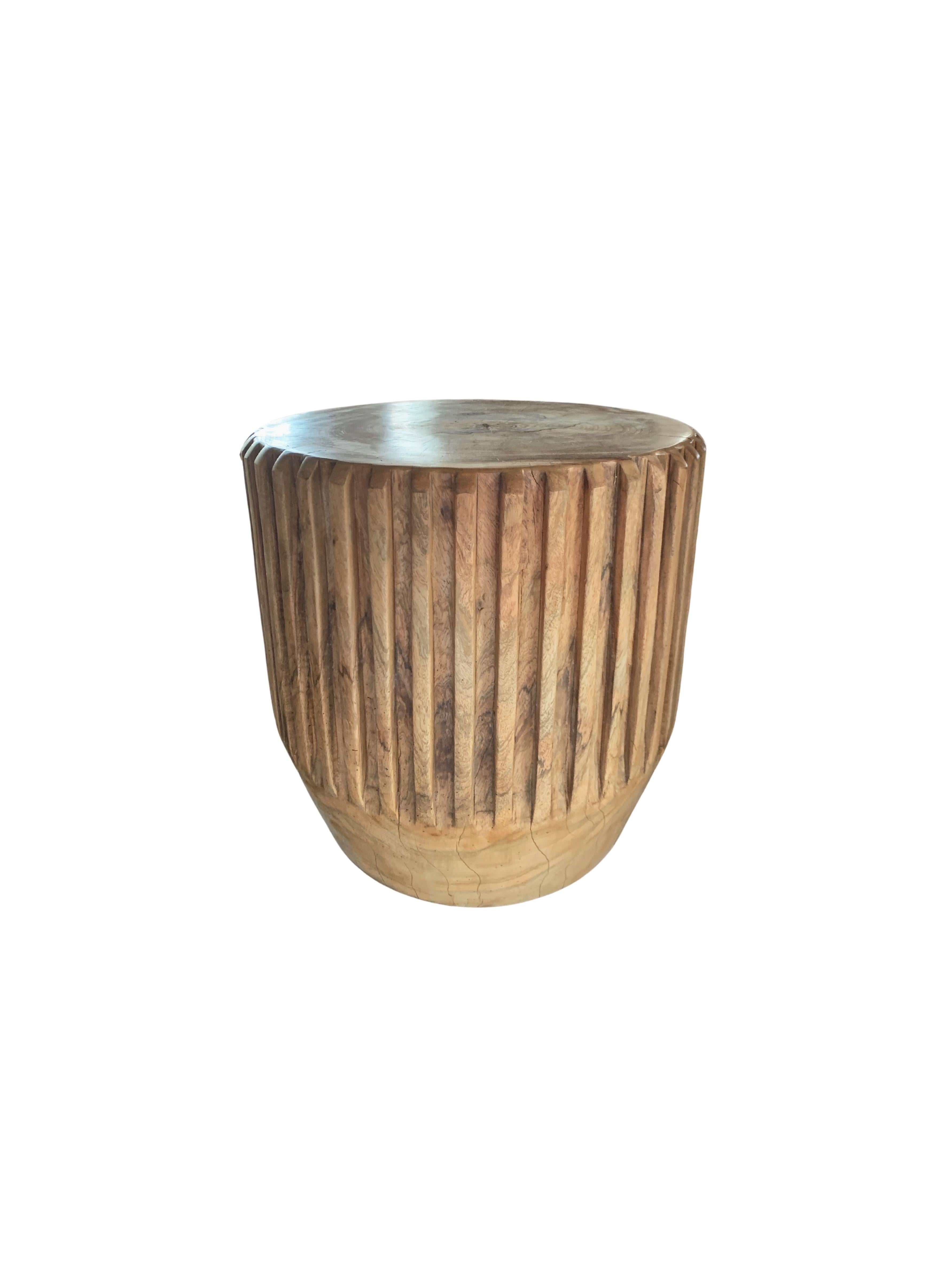 A wonderfully sculptural round side table with an engraved ribbed design on its sides. Its neutral pigments make it perfect for any space. A uniquely sculptural and versatile piece certain to invoke conversation. It was crafted from a solid block of