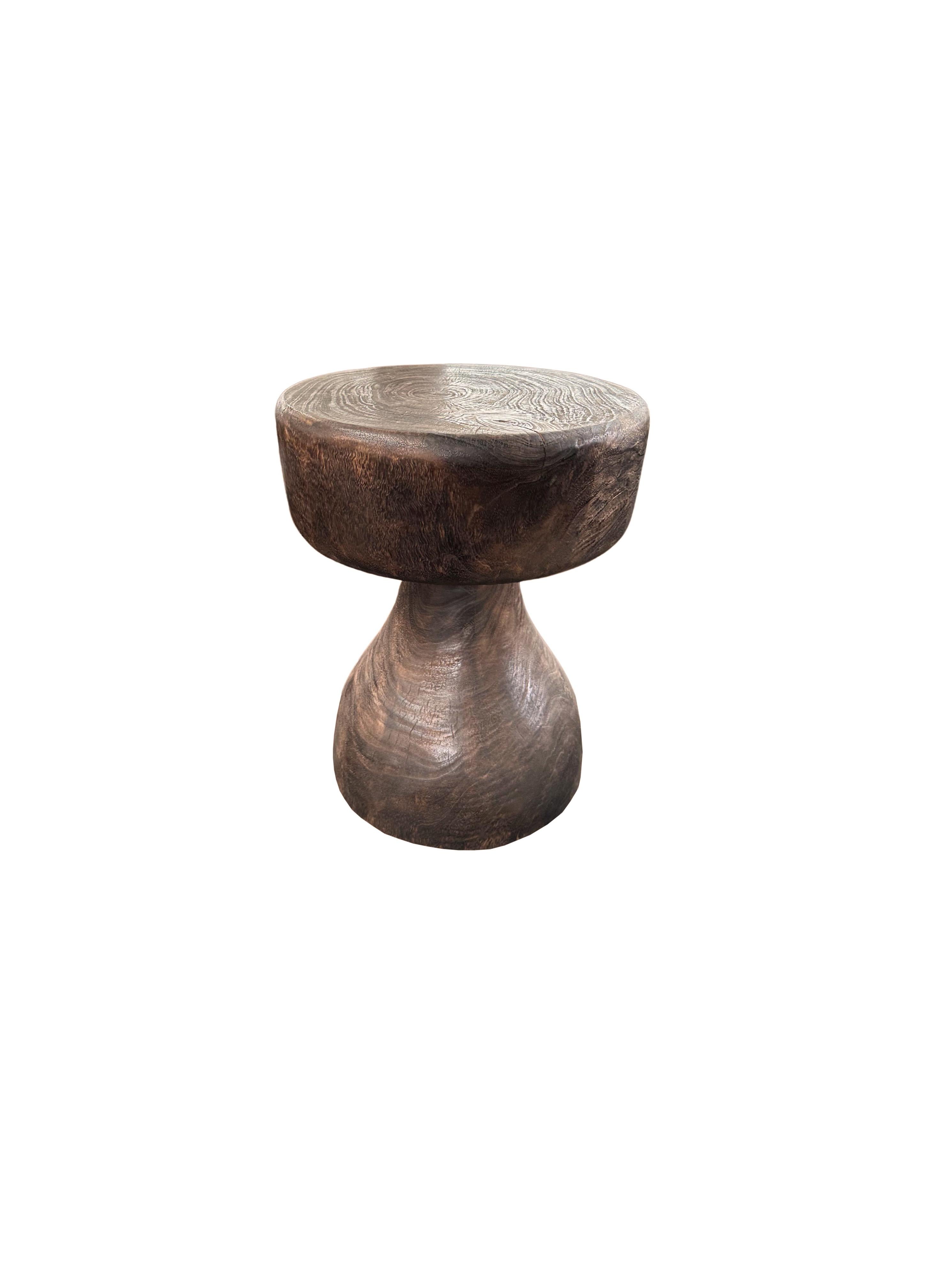 A wonderfully sculptural round side table, with an hourglass shape. Its neutral pigments make it perfect for any space. A uniquely sculptural and versatile piece certain to invoke conversation. It was crafted from a solid block of mango wood and has