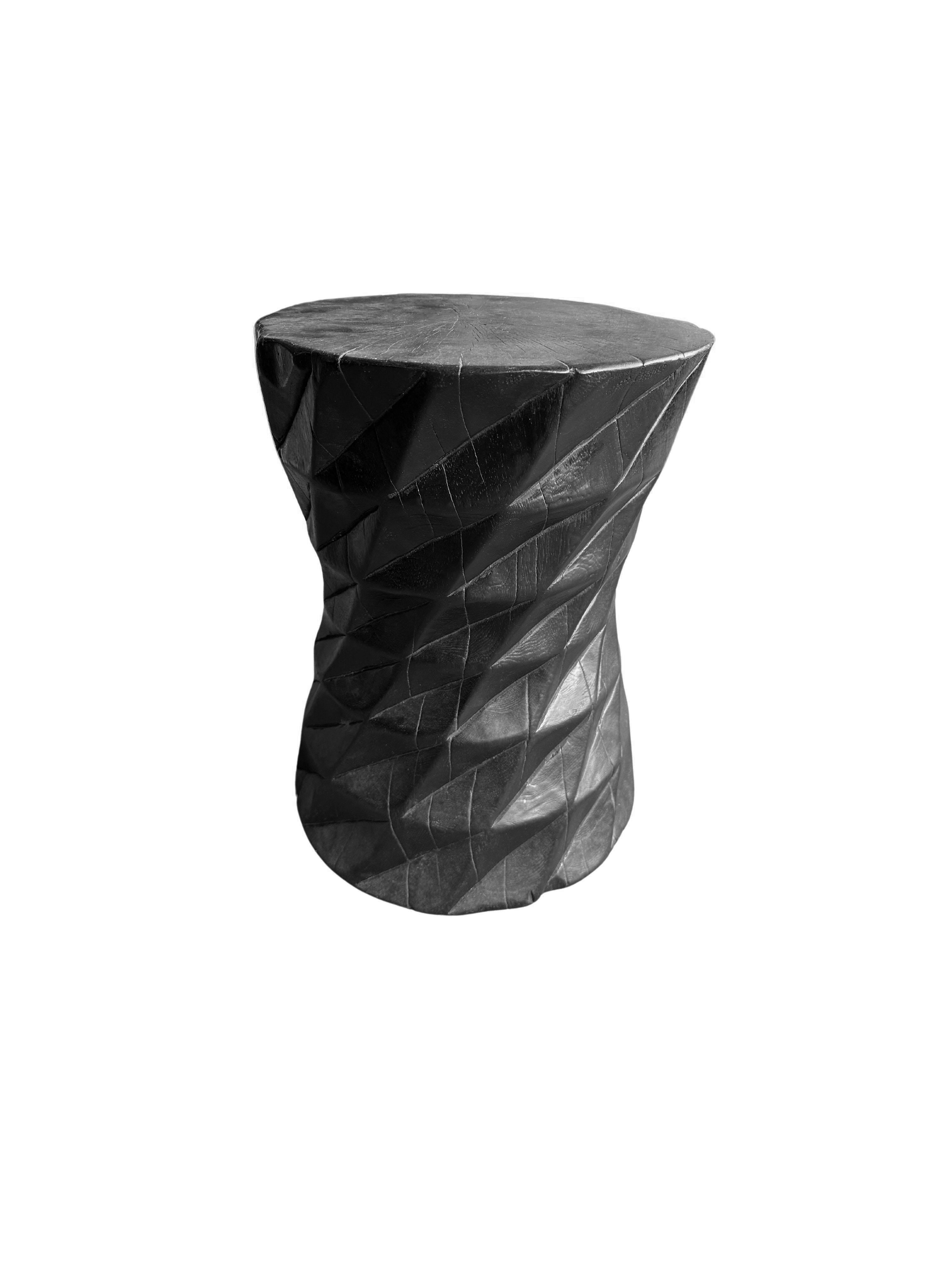 A wonderfully sculptural round side table. Its neutral pigments make it perfect for any space. It was crafted from a solid block of mango wood and features carved geometric detailing on its sides. To achieve is black color the wood was burnt three