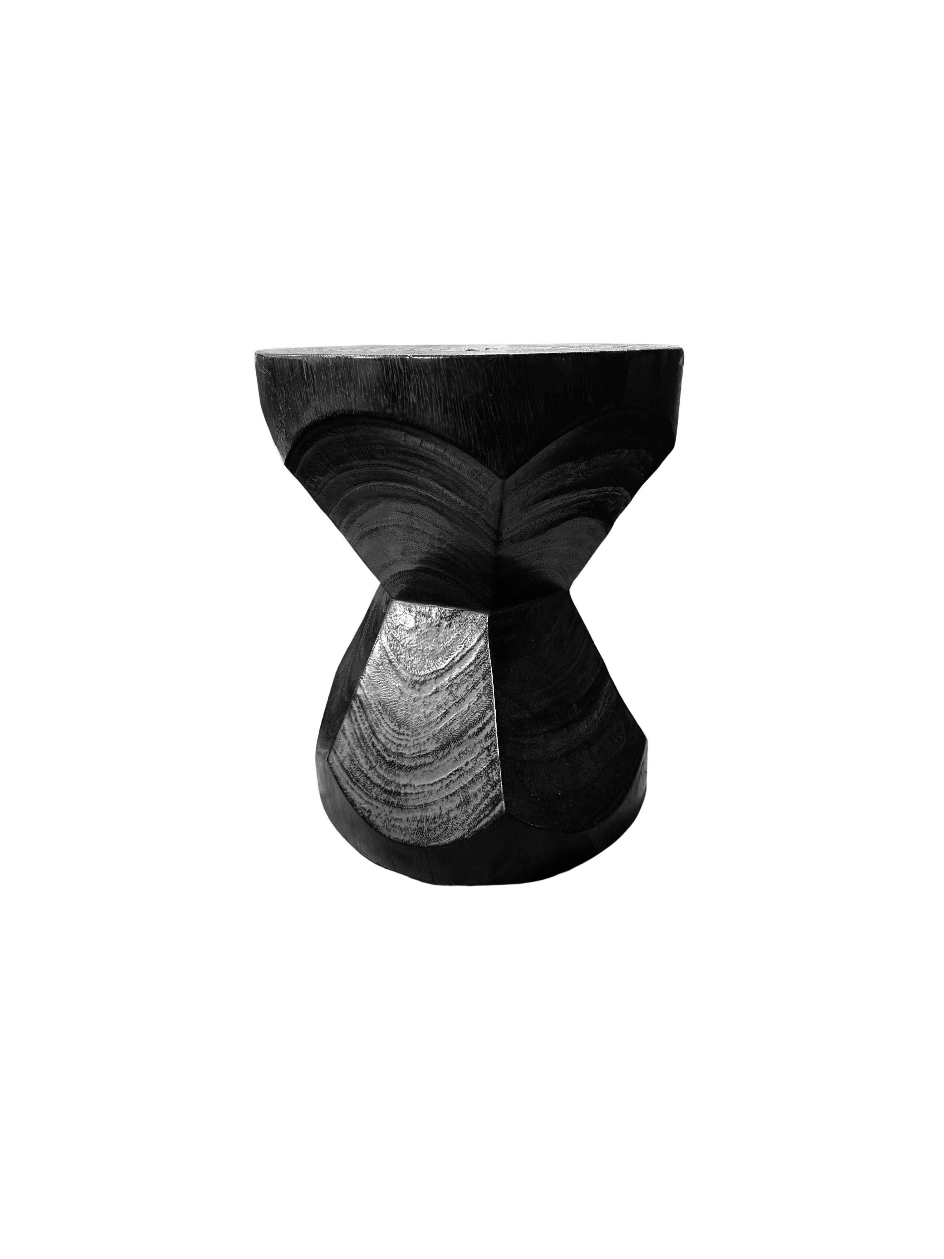 A wonderfully sculptural round side table. Its neutral pigments make it perfect for any space. It was crafted from a solid block of mango wood and features an elegant mix of curved and straight lines. To achieve its black color the wood was burnt