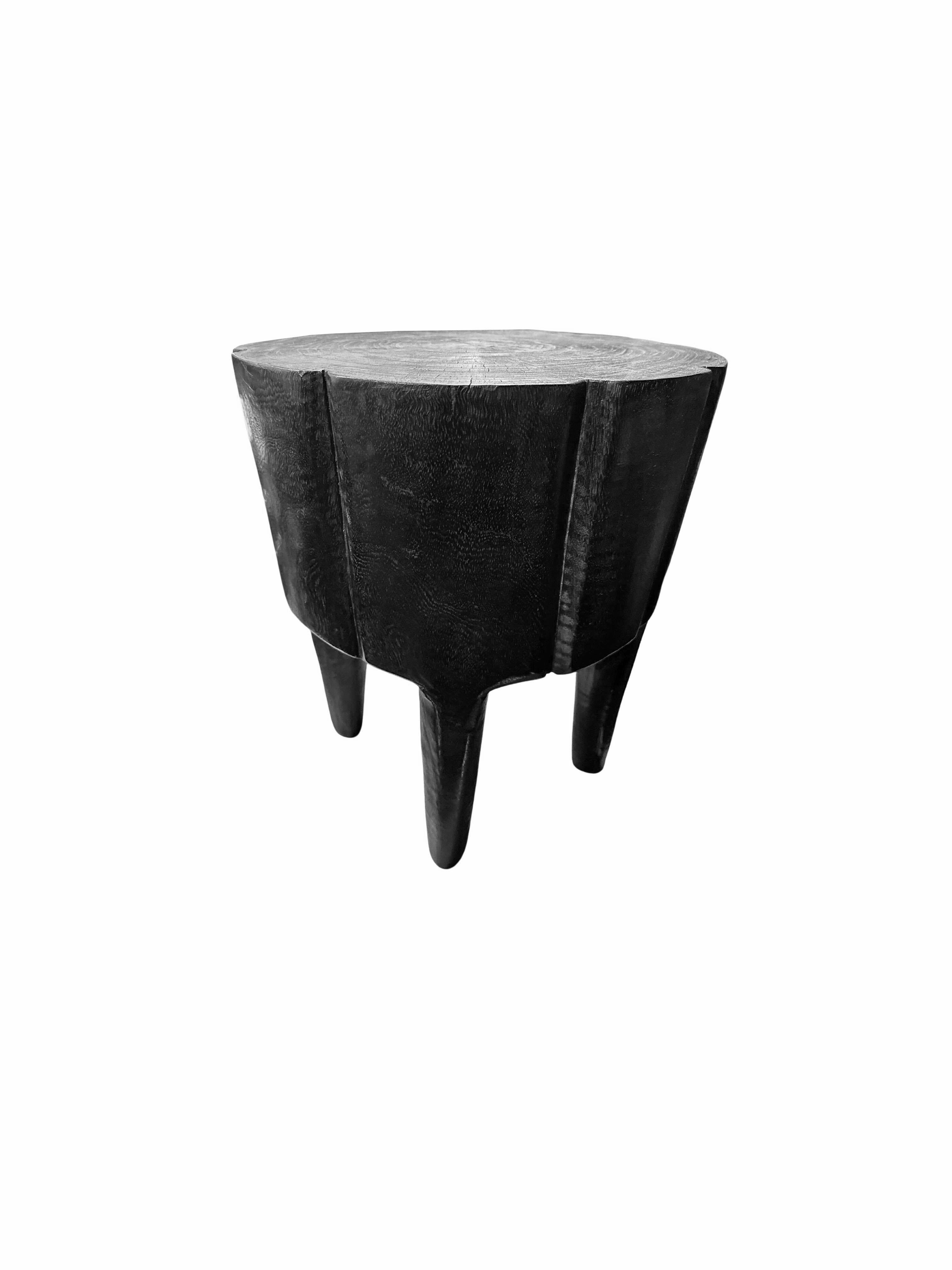A wonderfully sculptural round side table. Its neutral pigments make it perfect for any space. It was crafted from a solid block of mango wood and features subtle carved detailing on its side as well as slender legs. To achieve its black color the