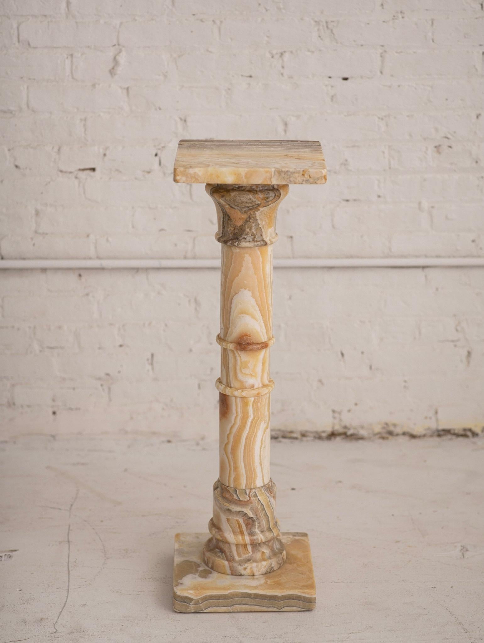 Neoclassical style marble pedestal. Heavy veining pattern ranging from caramels to beiges and browns. One solid piece.