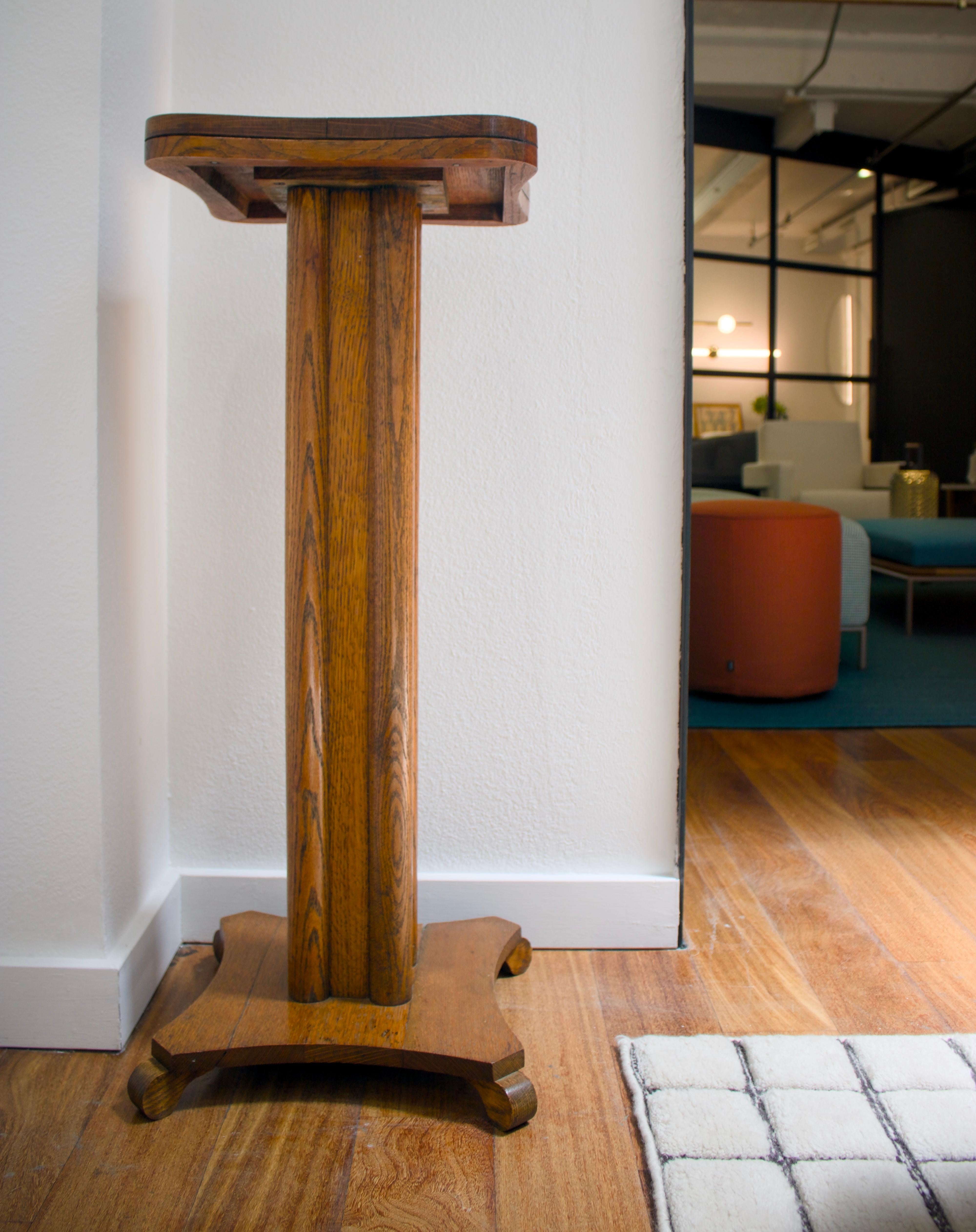 A 20th century solid oak pedestal featuring four legs and a rounded top.