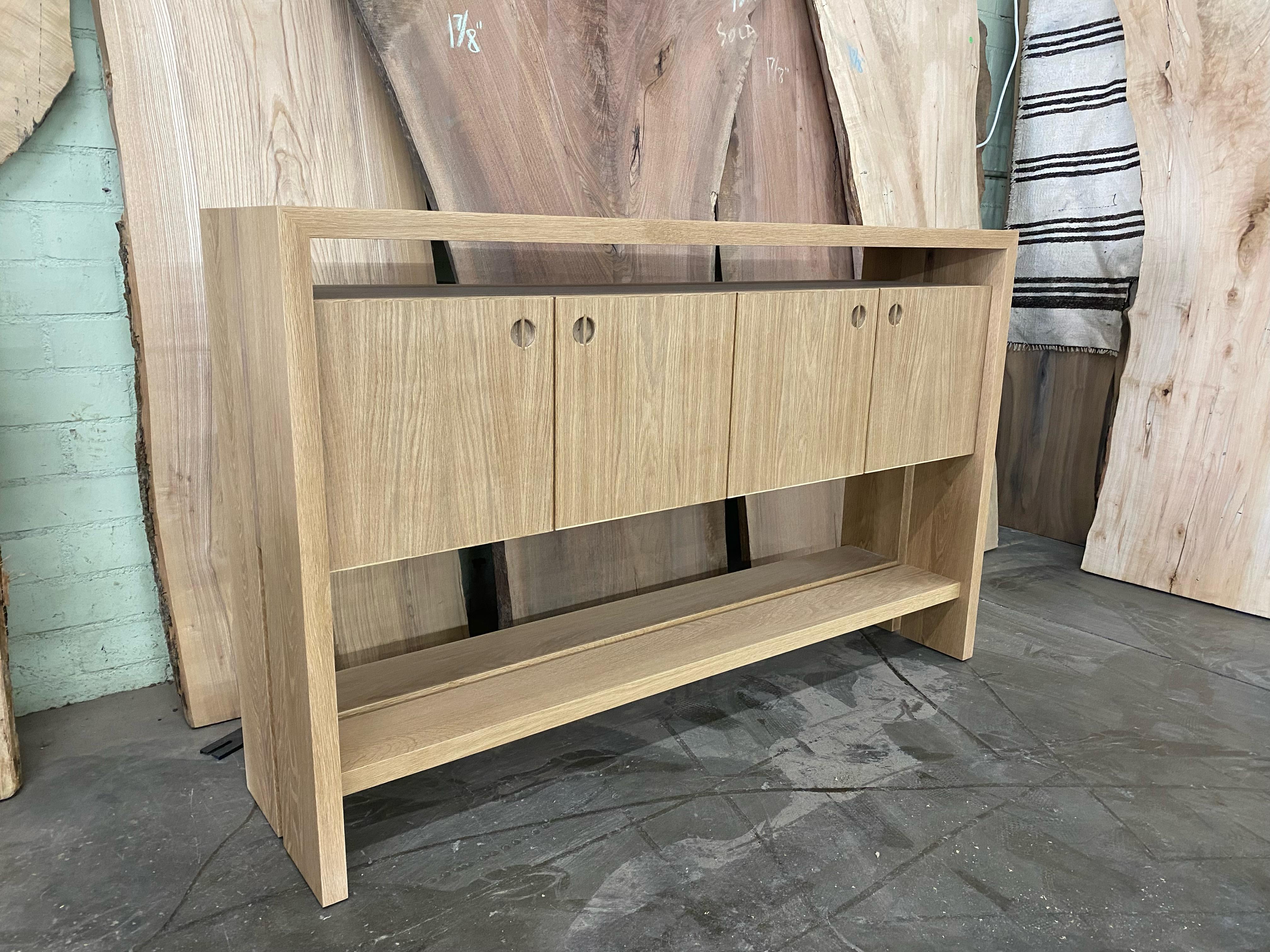 Questo tavolo con mobile in legno personalizzato è realizzato a mano negli Stati Uniti con una struttura interamente in legno duro. Presenta un design moderno con un corpo in rovere bianco massiccio e un intarsio minimalista in noce. Gli armadietti