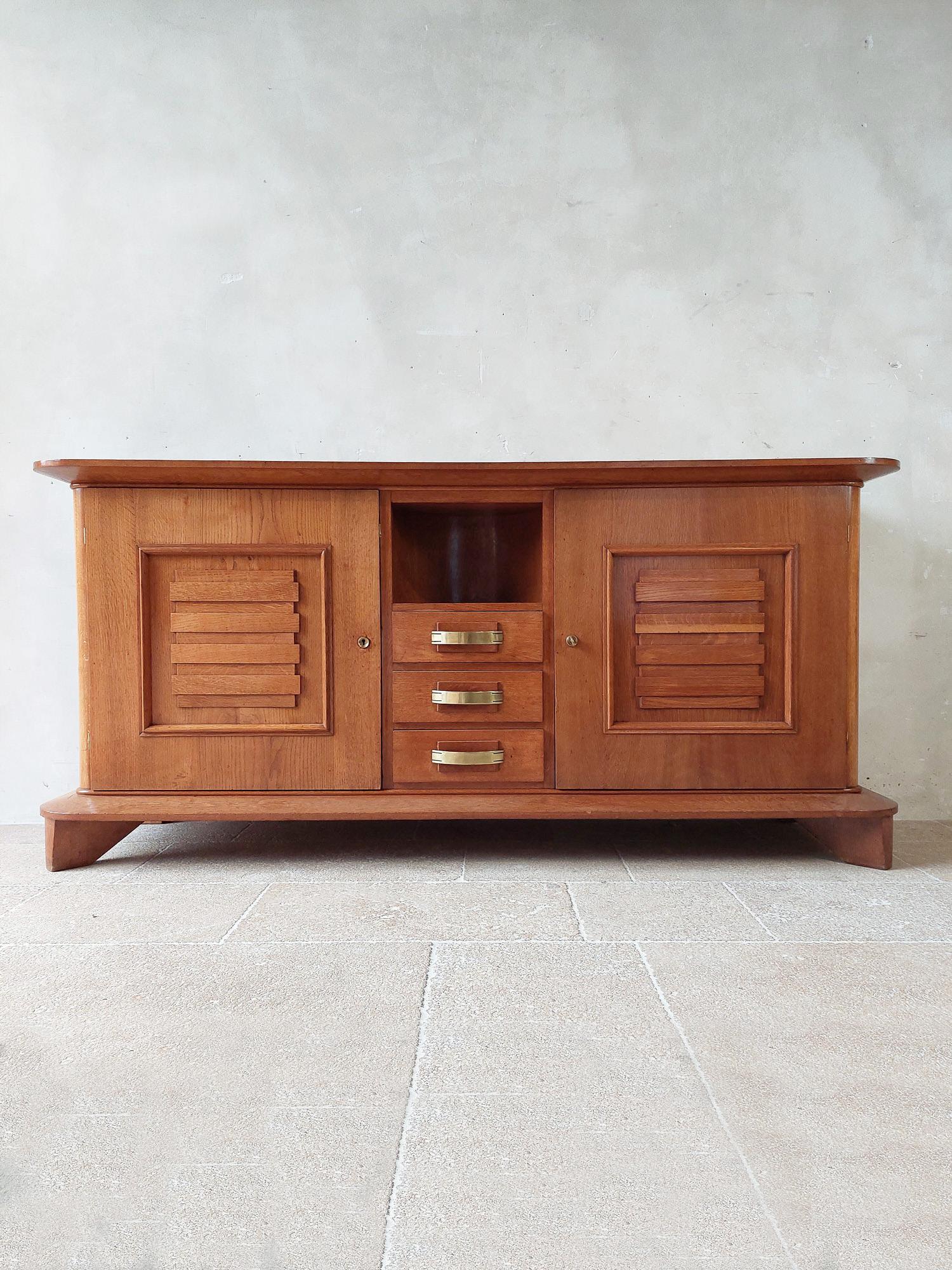 Vintage solid oak Art Deco sideboard by Jean Royere for maison Gouffé Paris, 1940. Two pannelend doors, in the middle 3 drawers with beautiful bronze handles underneath a curved niche.

Measures: H 100,5 x W 215,5 x D 50 cm.