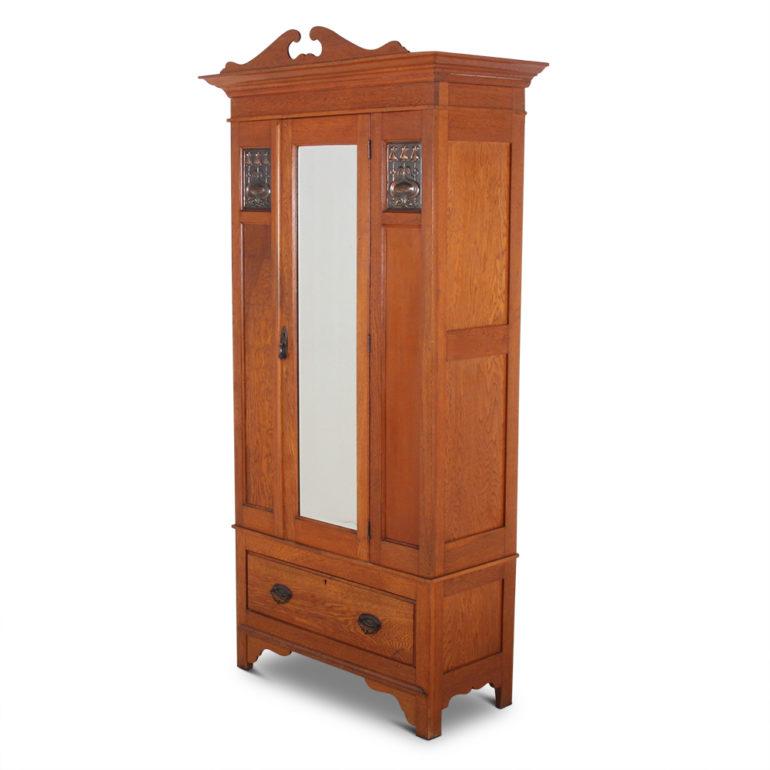 A small, English single-door wardrobe, the central door with bevelled mirror, the flanking panels each with hammered copper details. Lower drawer beneath cupboard.

  