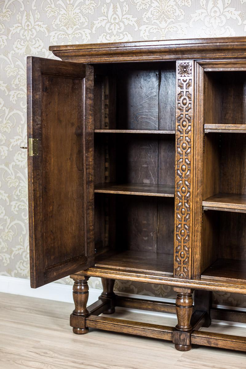 We present you this piece of furniture, circa 1940s, made of solid oak wood.

 The bookcase is supported on high, turned legs, which are connected at the bottom with moldings.

Two leaves of this piece of furniture are flanked by lesenes with