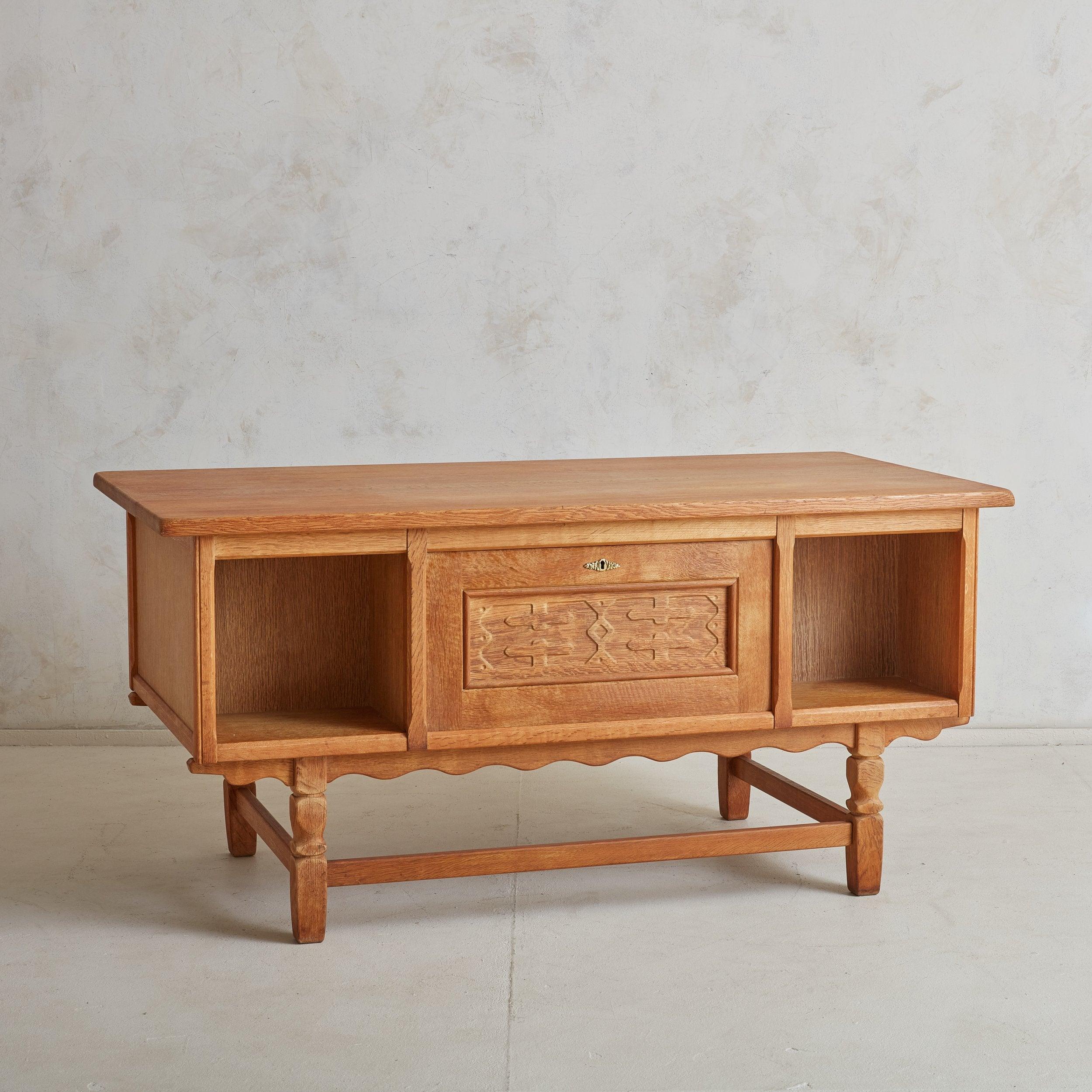 A charming rectangular executive desk attributed to Danish furniture designer Henning Kjærnulf. The Mid Century-Modern, Baroque-inspired silhouette is constructed of warm, solid oak and features a scalloped apron, sculpted legs, hammered gold-tone