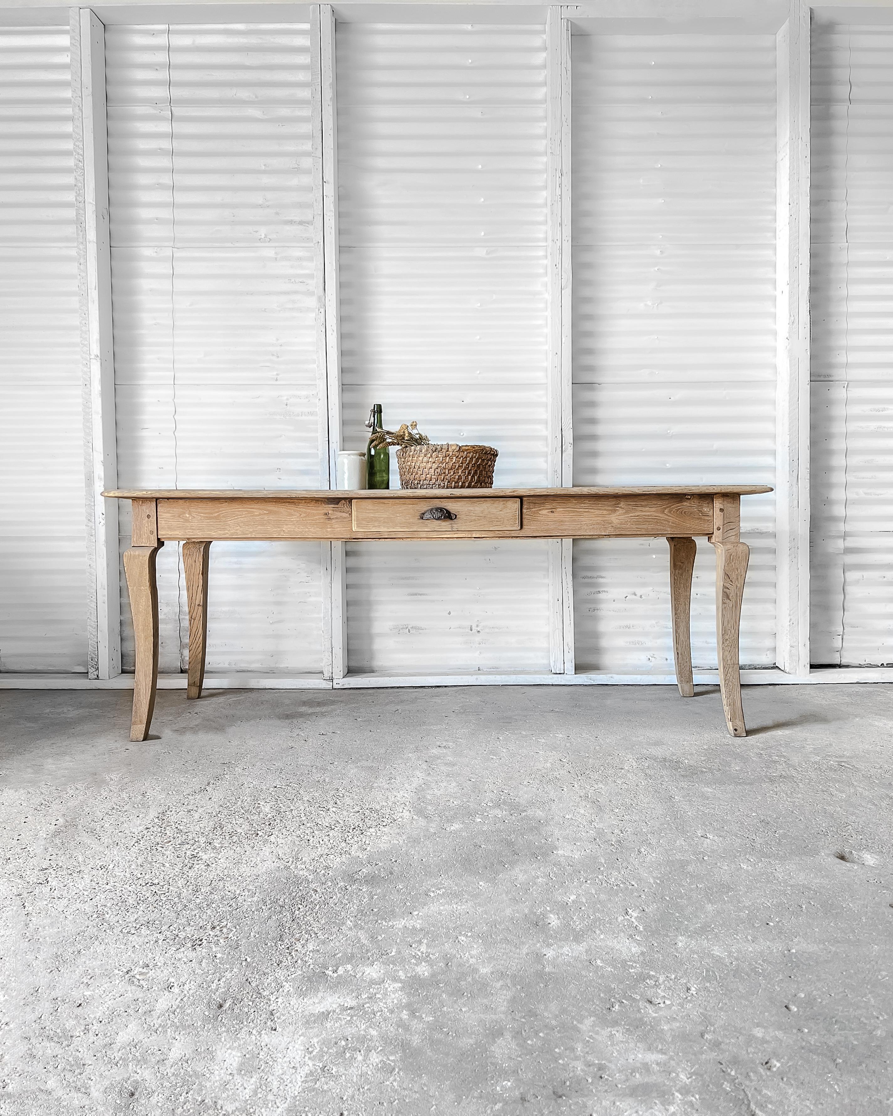 A gorgeous, solid oak dining table with a natural, raw wood finish, soft beveled edge top, functional drawer (with original iron cup pull), and graceful cabriole legs. Well-done extensions have been added to the foot of each leg to raise the height