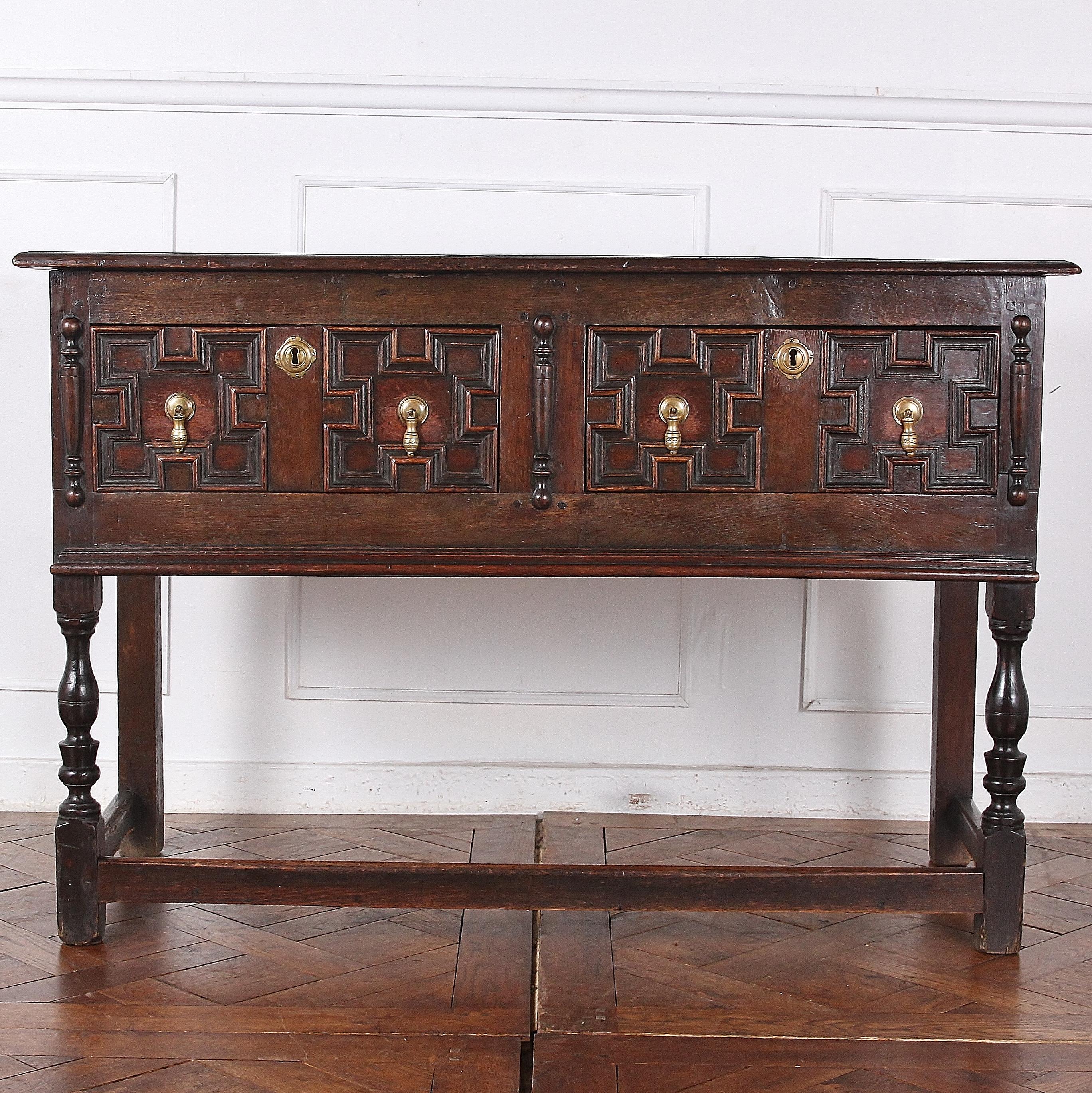Solid oak Jacobean-style dresser or server with paneled drawer fronts and brass drop pulls, the whole raised on turned legs united by an oak stretcher. The piece has a deep warm color and mellow patina. Sturdy and suitable for everyday use.