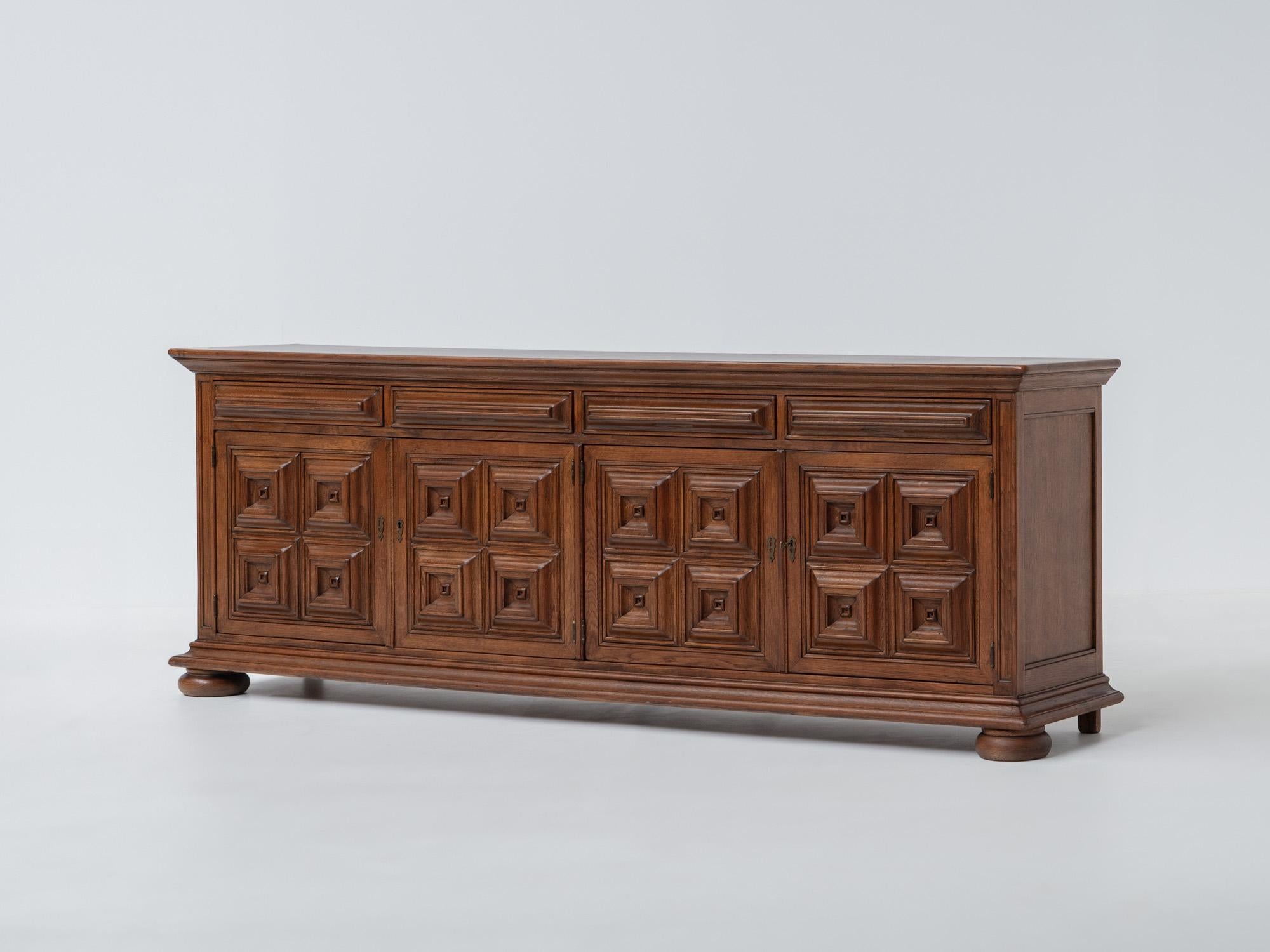 Ce buffet espagnol en chêne massif des années 1940 présente le charme intemporel de l'artisanat rustique. Fabriquée en chêne richement grainé, cette pièce présente une construction robuste avec des panneaux géométriques audacieux sur les portes,