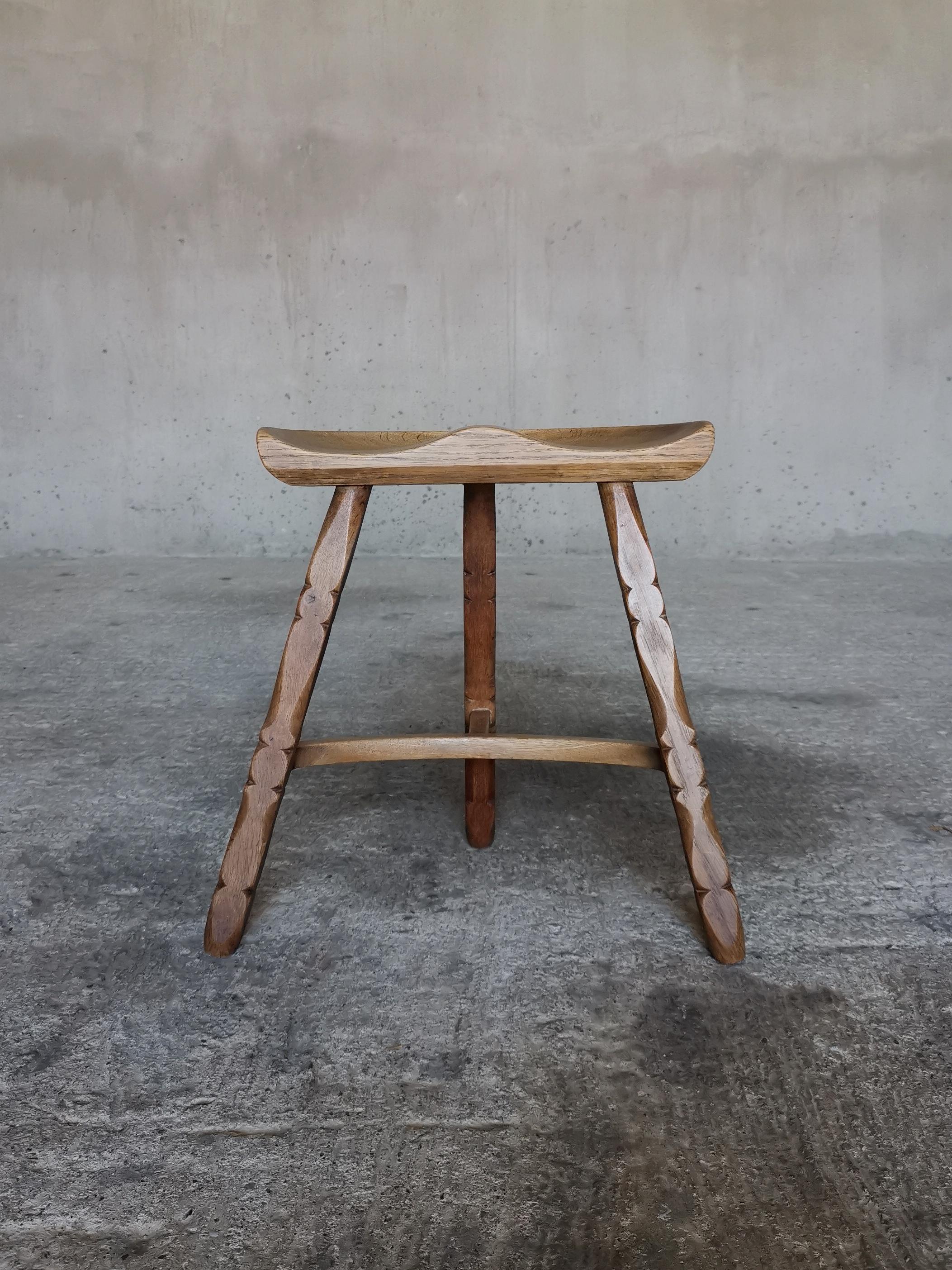 This Danish 1960s tripod stool in solid oak has turned legs with decorative details  similar to works of Danish designer Henning Kjærnulf.
The notable and comfortable seat is carved from thick solid Danish oak. The stool has a deep and rich oak