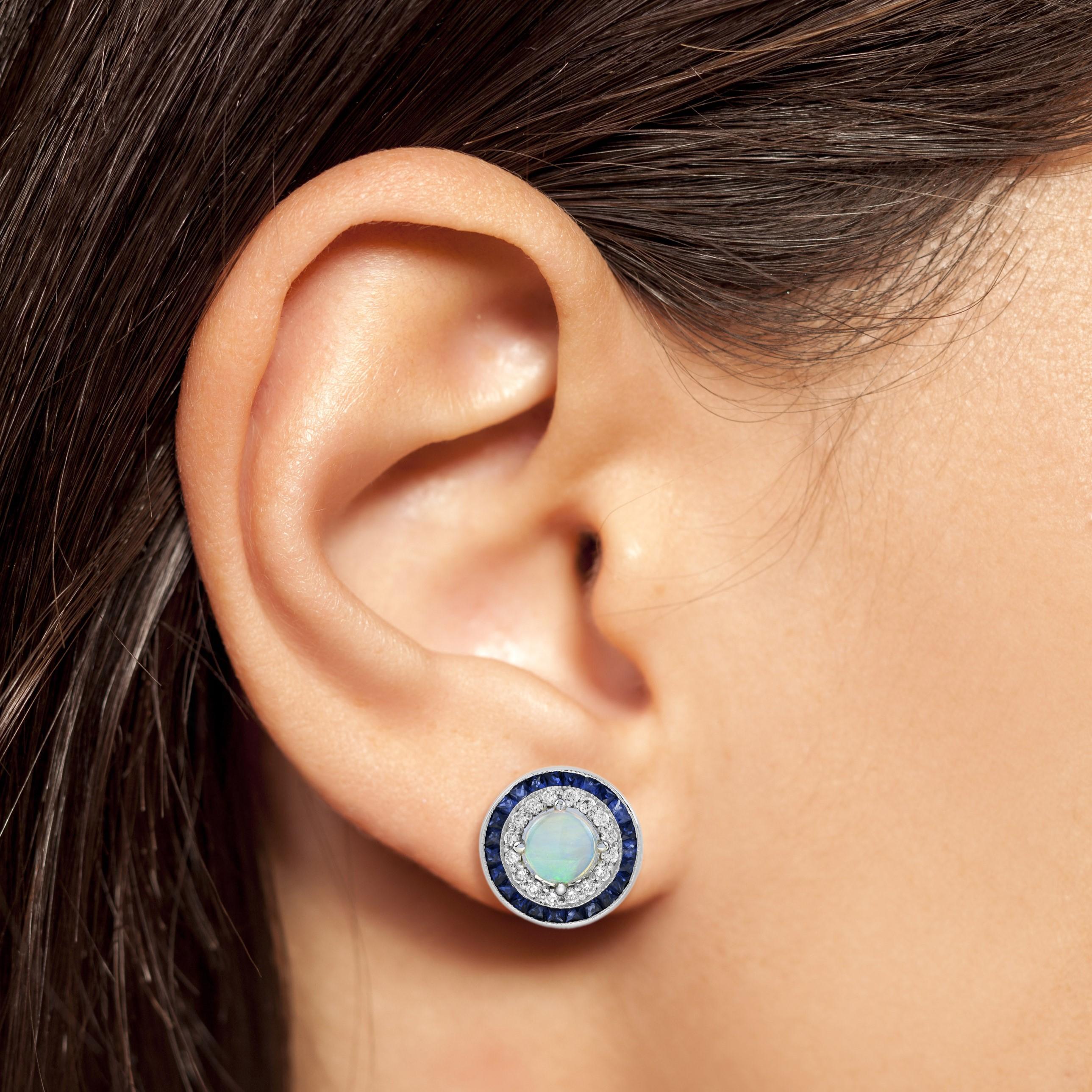 These Art-Deco stud earrings are completely spectacular! The sparkling diamonds and vibrant blue sapphires surround the excellent play of color center opal, which is in a thin bezel with millgrain detail. Crafted in 18k white gold.

Earrings