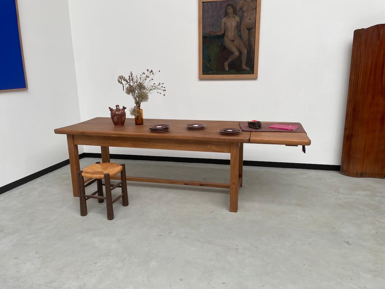 Très jolie table en pin massif des années 1950, qui passe de 2 mètres à 250 cm en un clin d'œil grâce à sa rallonge. Ses lignes épurées et ses courbes le rendent irrésistible. Avec sa base imposante et son plateau épais, il est très robuste et