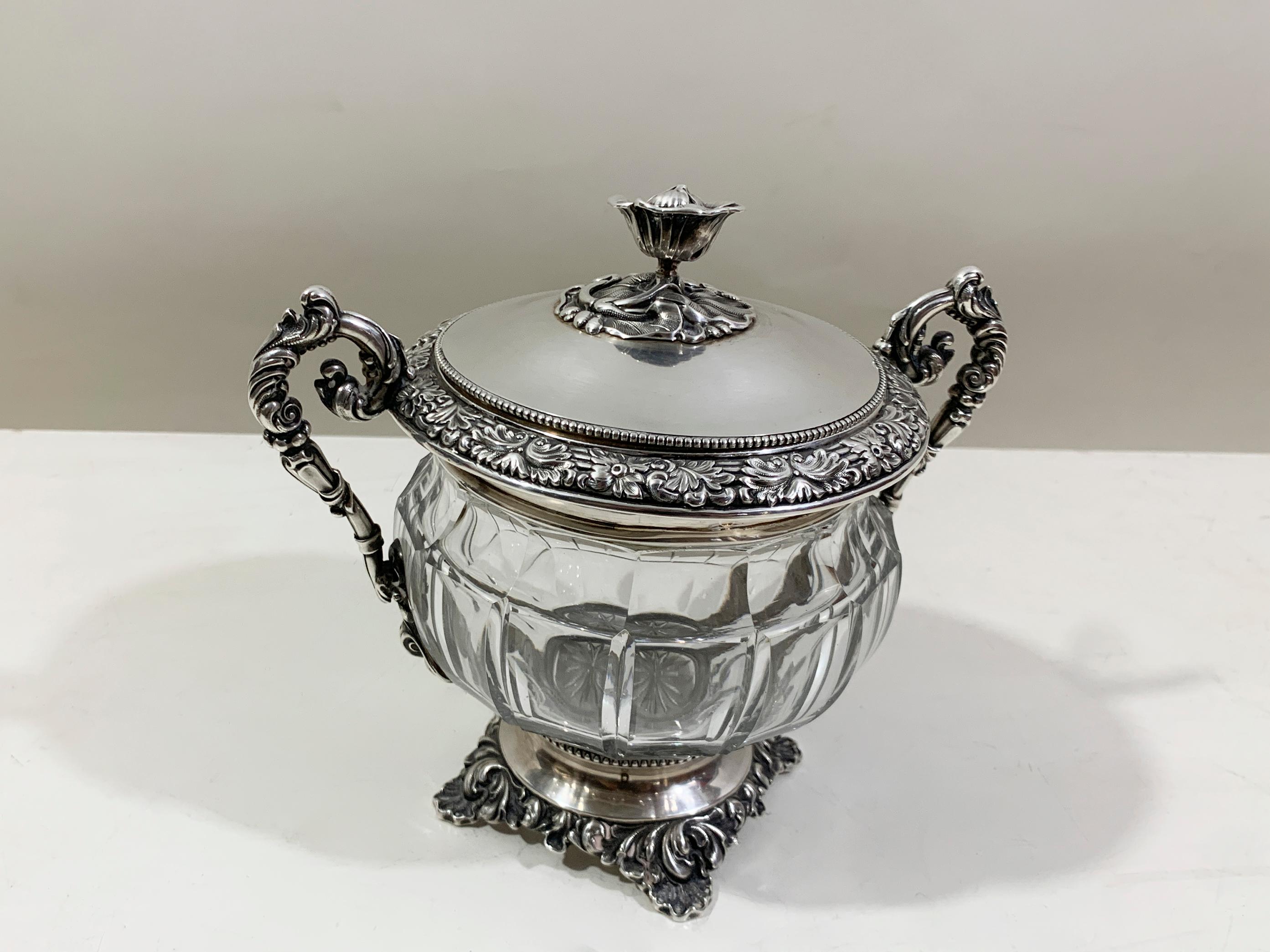 Cette exquise coupe française à couvercle est un superbe exemple d'art décoratif du début du XXe siècle. La pièce présente une superbe coupe en cristal taillée à la main, avec un design nervuré et à panneaux, placée dans un cadre en argent massif