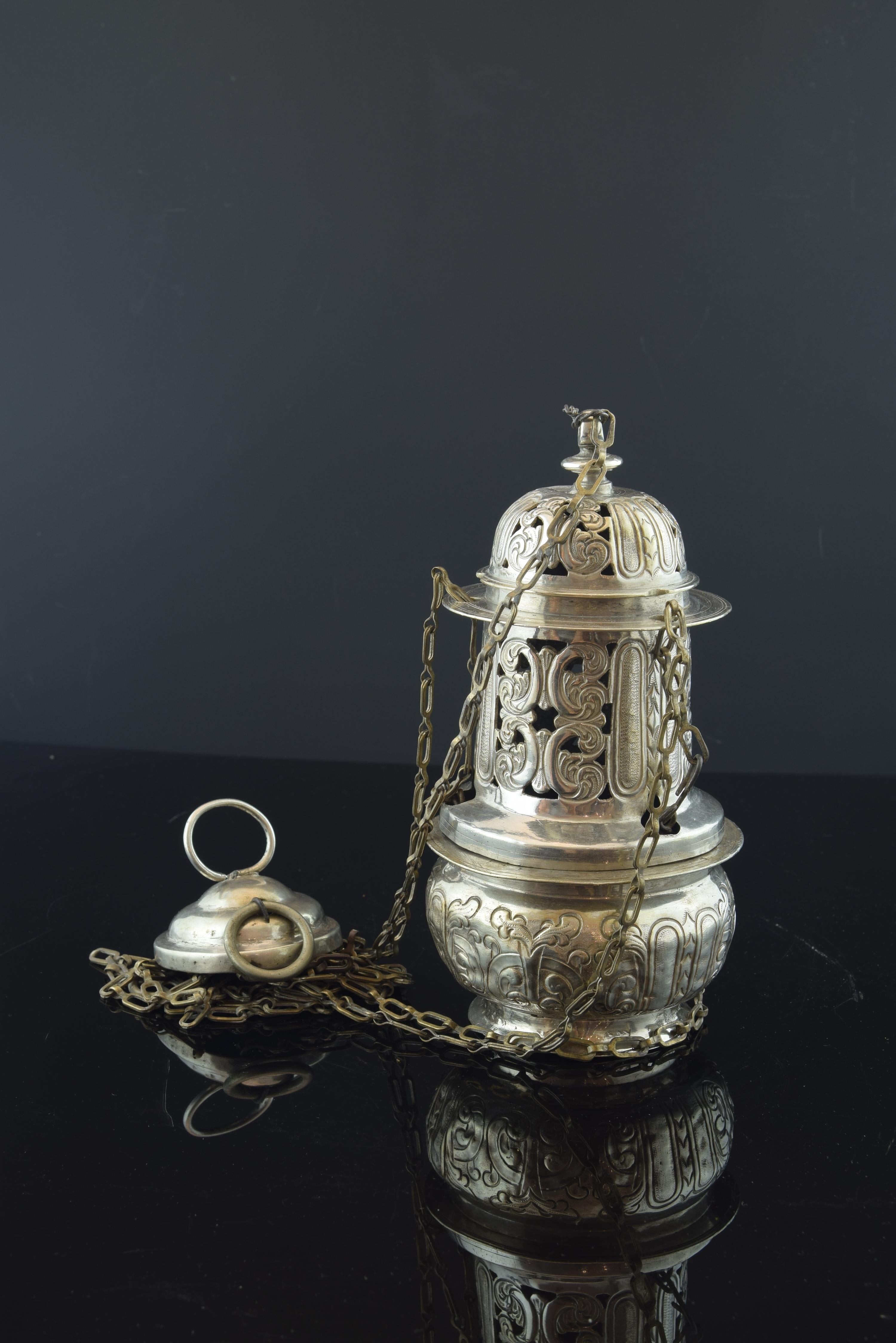 No hallmarks.
Liturgical censer made of silver composed of a piece with ring that is attached to the main body of the object by chains of elongated links. This body has a rectangular shape in the centre, circular at the top and the base, and a