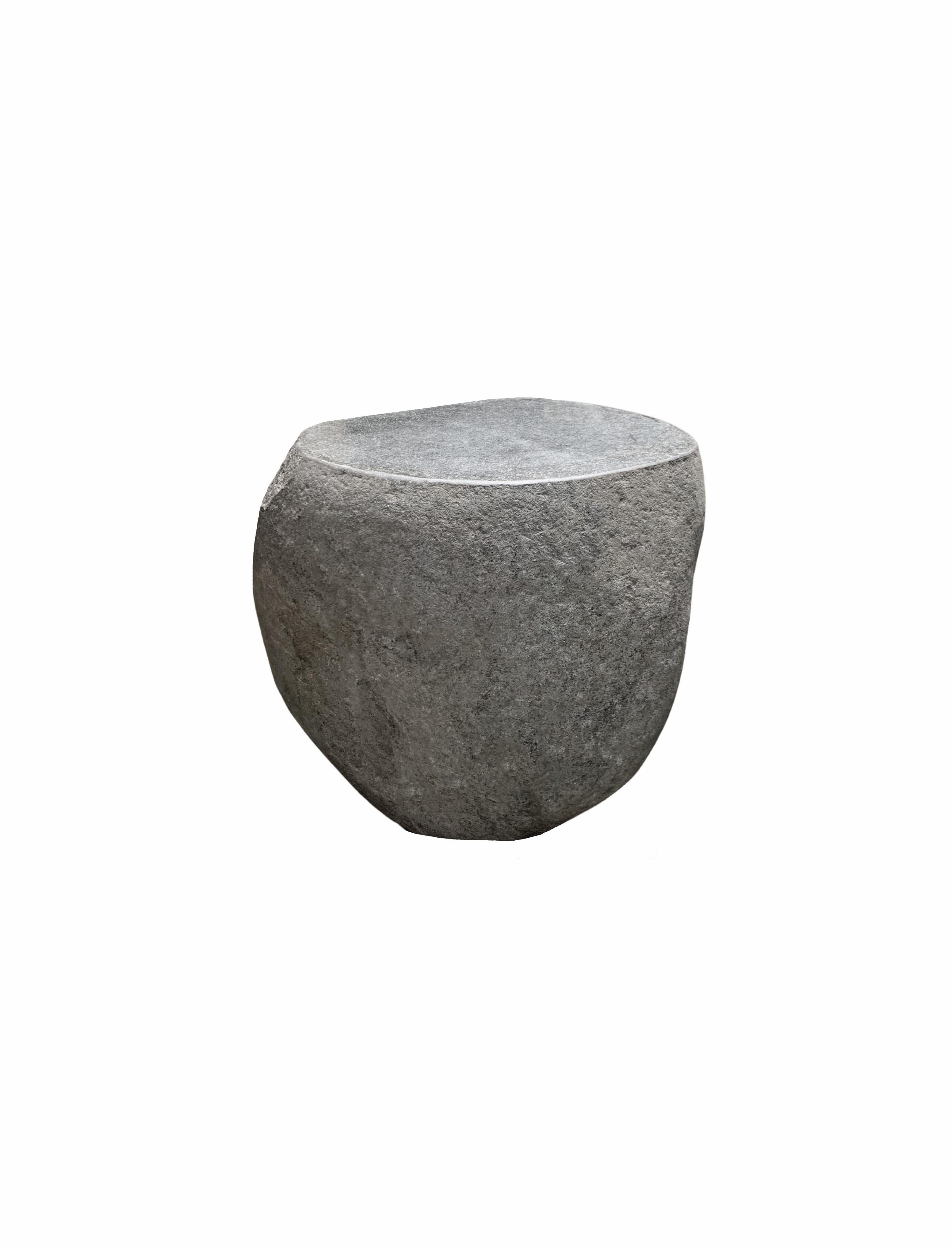 A incredibly heavy and solid rounded stone side table / pedestal. This lovely sculptural object was crafted from a solid stone sourced from a river bed in East Java. A raw and organic object with beautiful textures. Its top side was carved, sanded