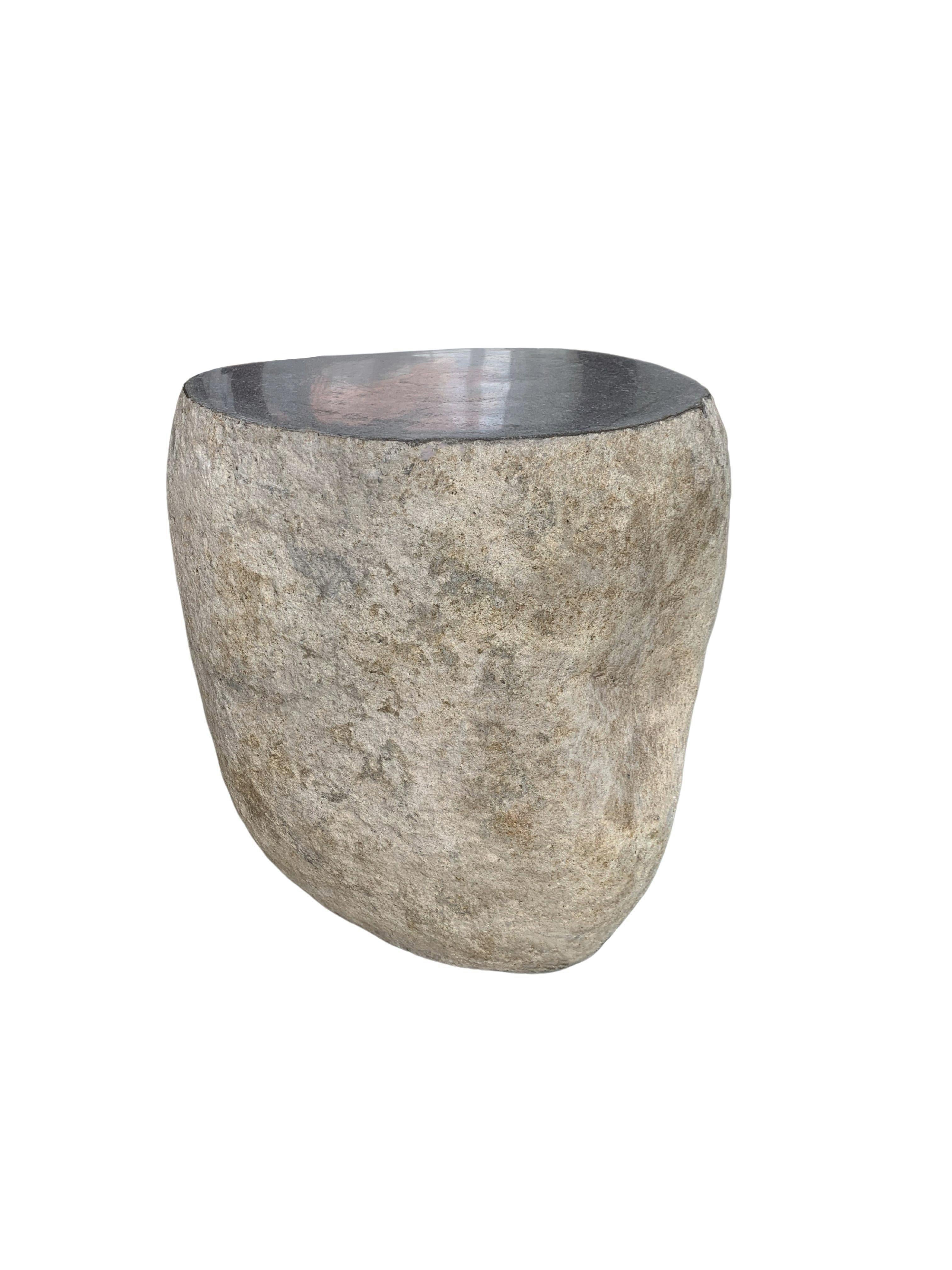 A incredibly heavy and solid rounded stone side table / pedestal. This lovely sculptural object was crafted from a solid stone sourced from a river bed in East Java. A raw and organic object with beautiful textures. Its top side was carved, sanded