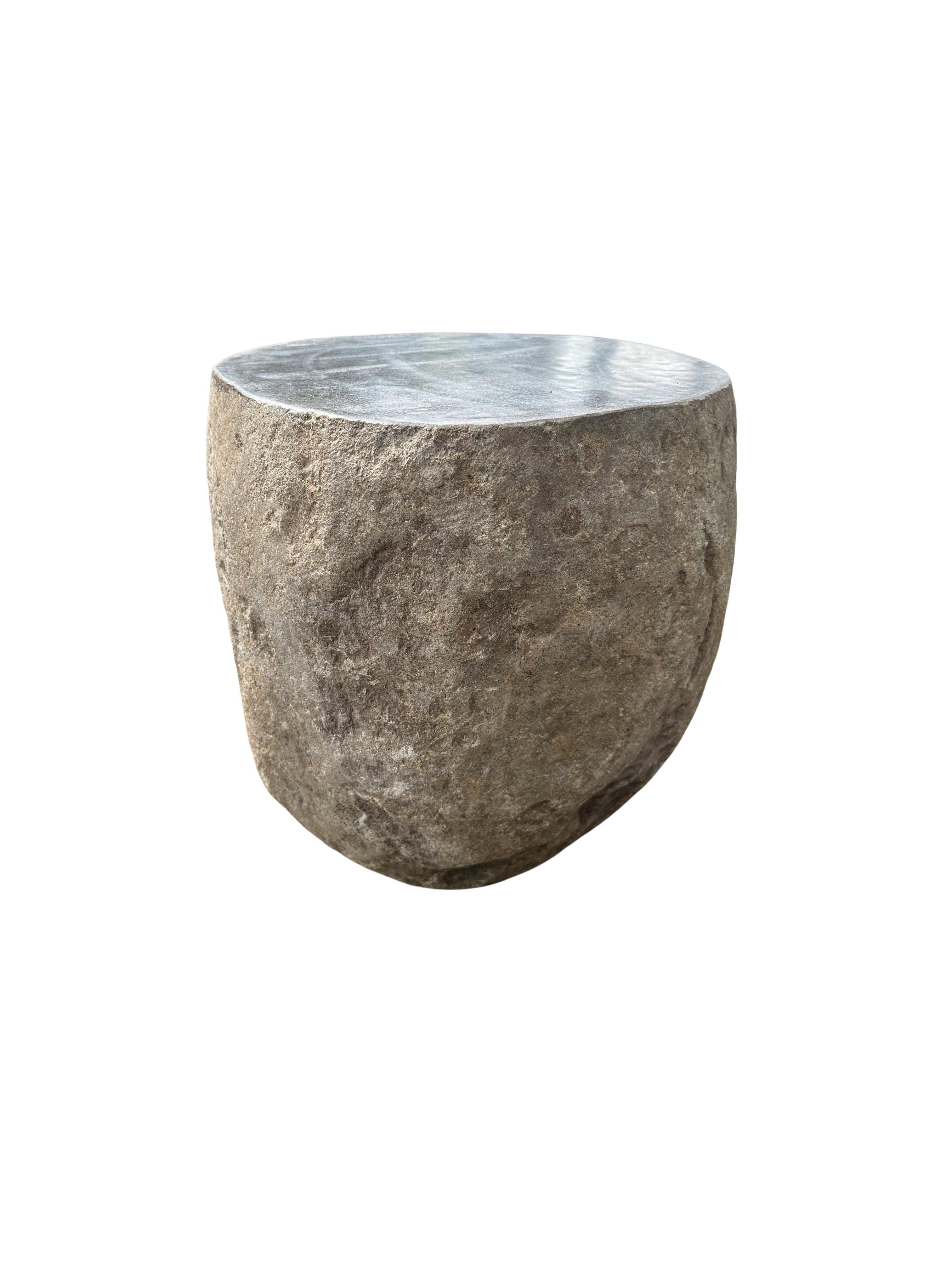 A incredibly heavy and solid rounded stone side table / pedestal. This lovely sculptural object was crafted from a solid stone sourced from a river bed in East Java. A raw and organic object with beautiful textures. Its top side was carved, sanded
