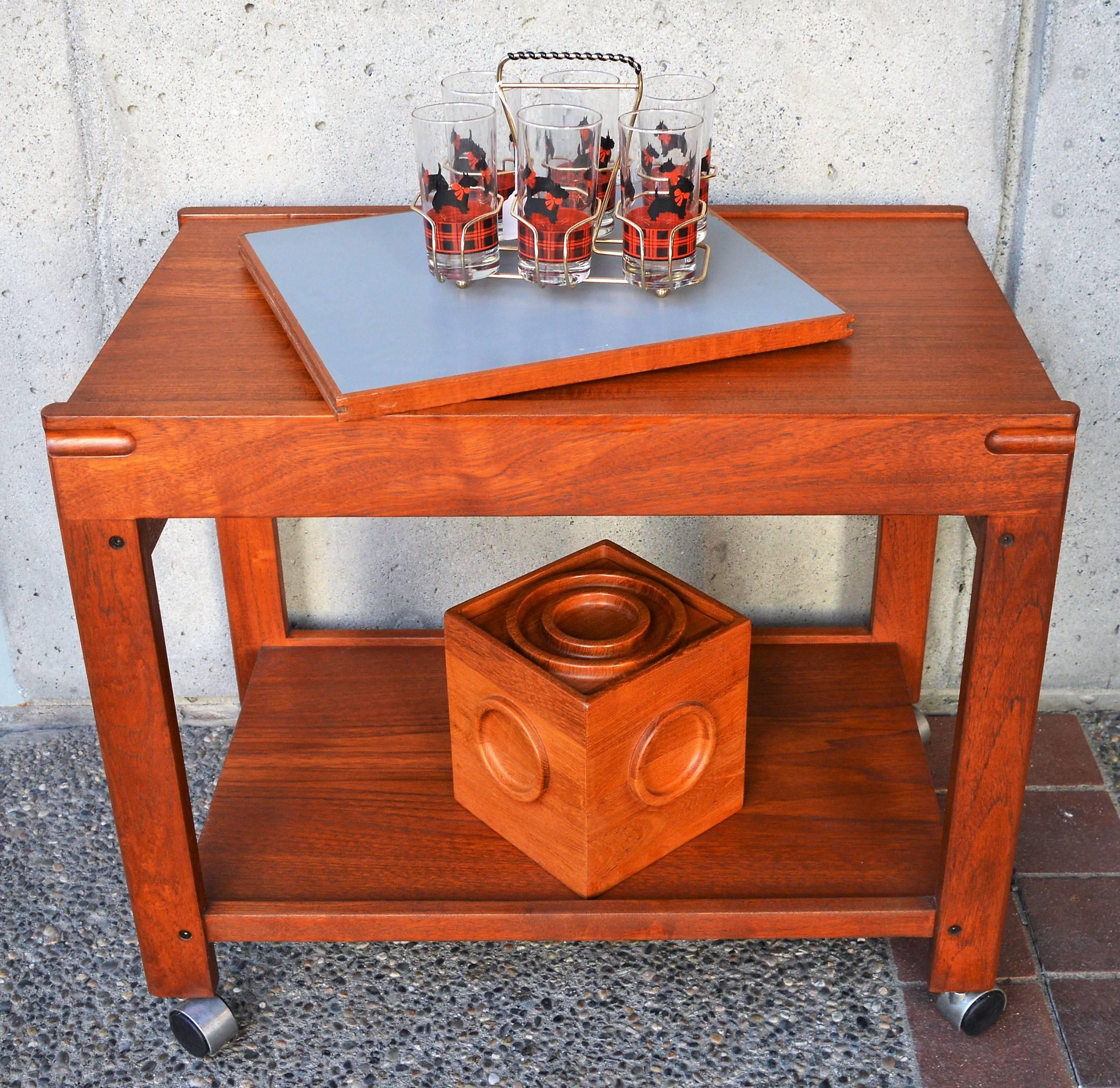 This lovely Danish modern teak bar cart or serving table was designed by Aksel Kjersgaard in the 1960s and features a top that slides over to accommodate an extension leaf that lives underneath - which is grey on one side and white on the other. On