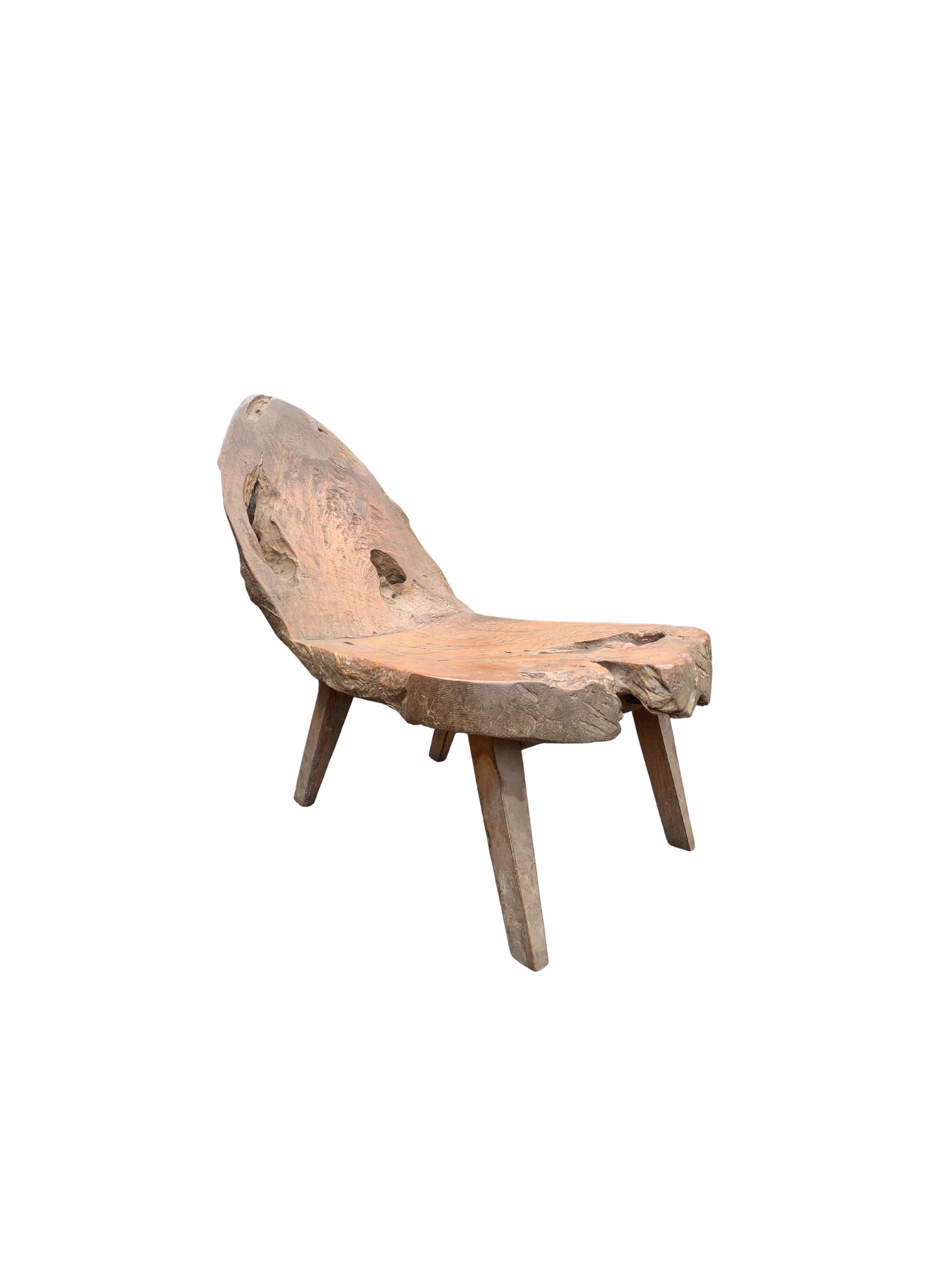 This hand-carved teak wood chair originates from the Island of Madura, off the coast of Northeastern Java. It features a wonderful organic shape with angular legs. The mix of textures, shapes and holes add to its charm. The seat and backrest was