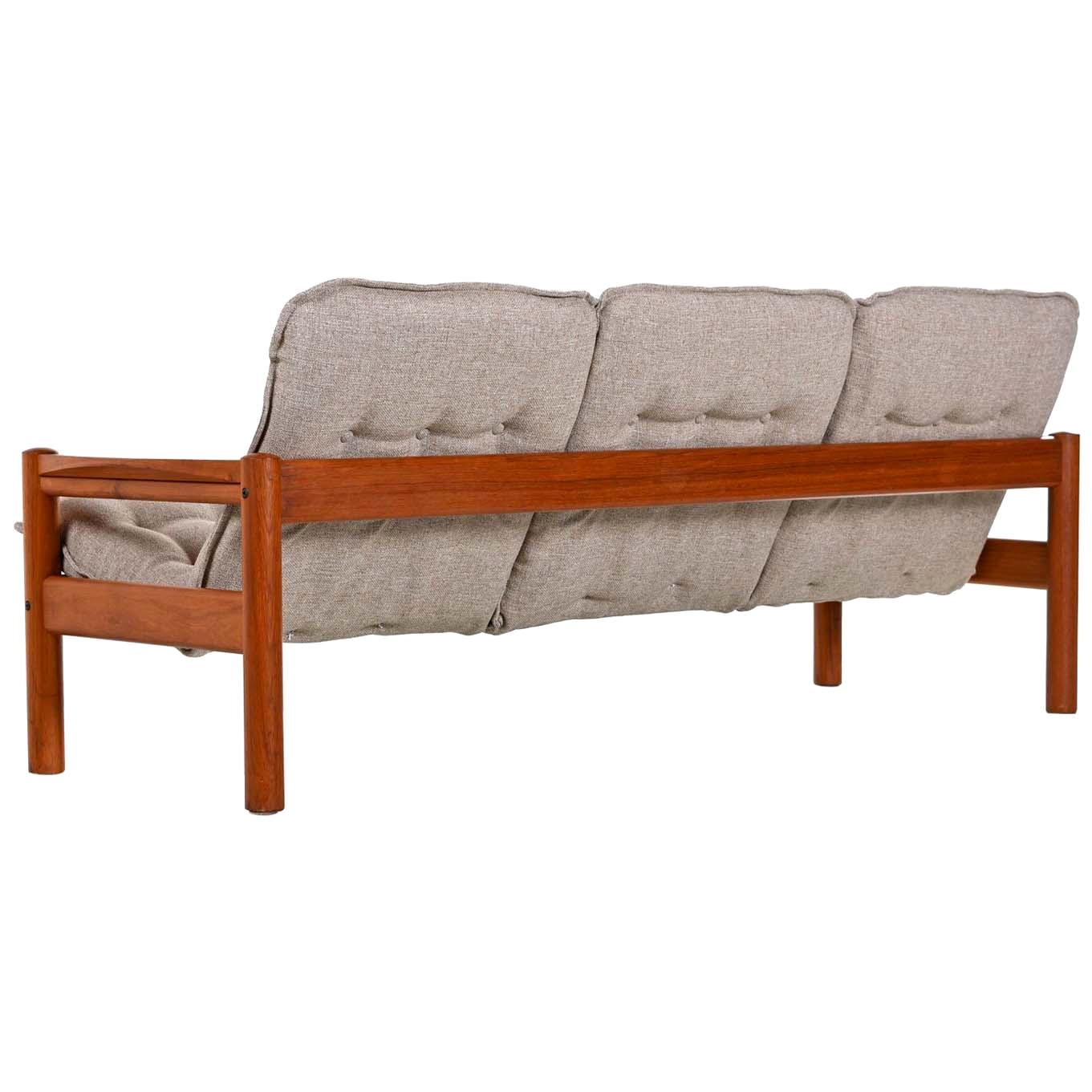 Domino Mobler 3-seat solid teak sofa couch restored to near mint condition. Solid teak frame with rigid construction. The sculpted arms stand out within the sleek, Minimalist, modern, low profile design. Fresh new upholstery, button tufted in the