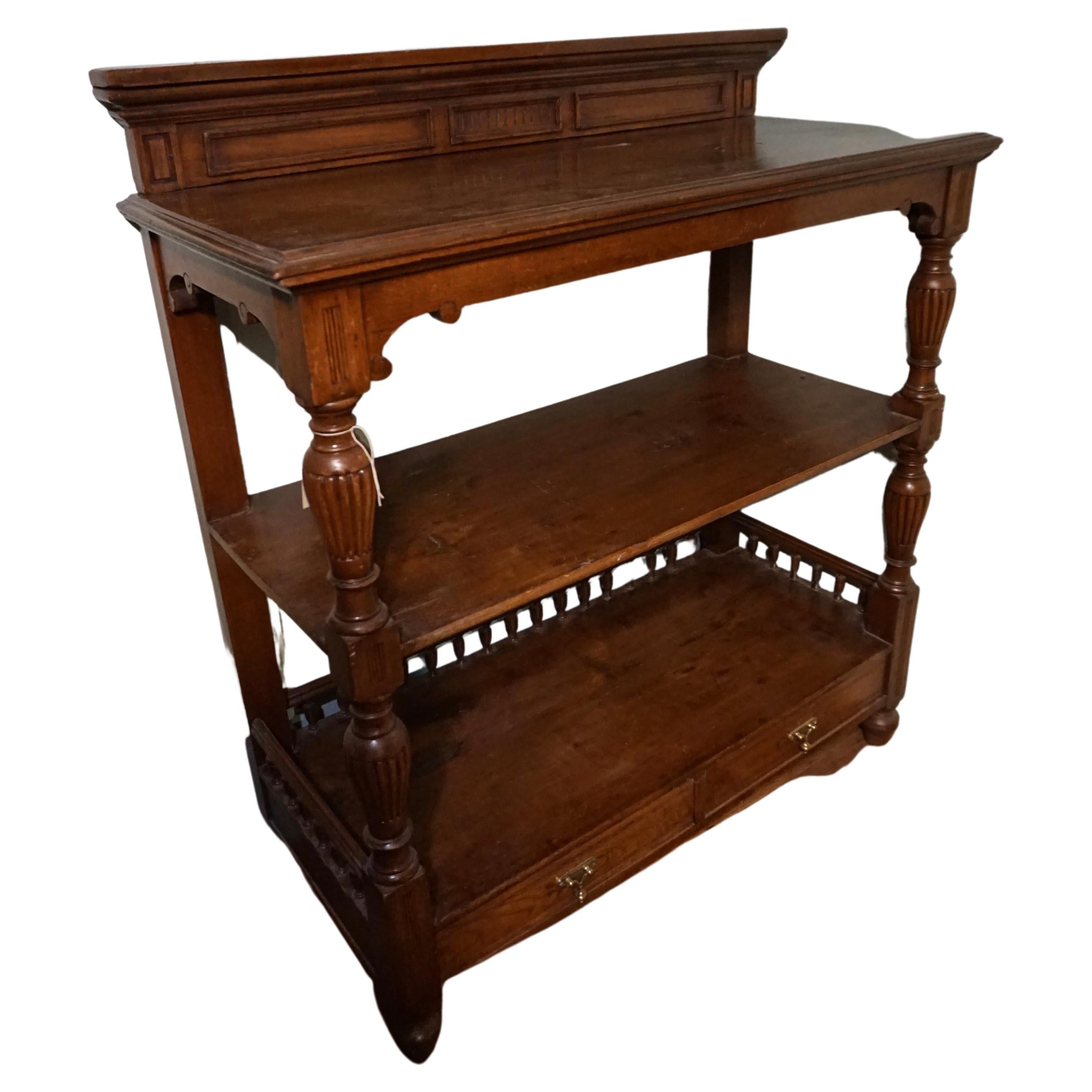 British Colonial solid Teak whatnot stand with shelves in good condition. Hand carved fluted vase columns with crown moulding and drawers. Brass hardware with tear drop handles. Aesthetic and functional piece which can be repurposed as a TV stand,